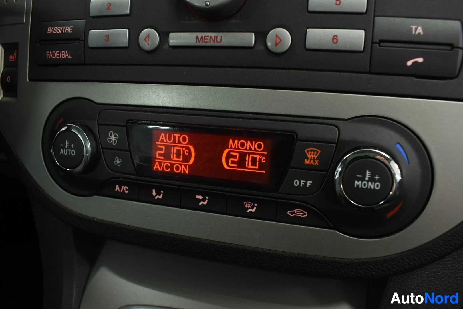 Yksityiskohta: Auton ilmastointilaitteen paneeli ja lämpötilan säätimet keskikonsolissa. Näytössä lukee "AUTO 21.0°C A/C ON" ja "MONO 21.0°C".