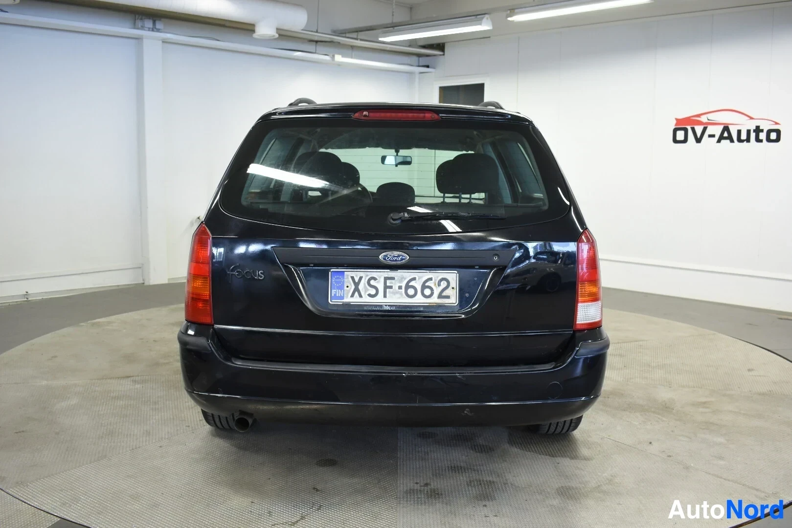 Takaa: Musta farmariauto kuvattuna suoraan takaa. Autossa on kattokaiteet ja rekisterinumero on