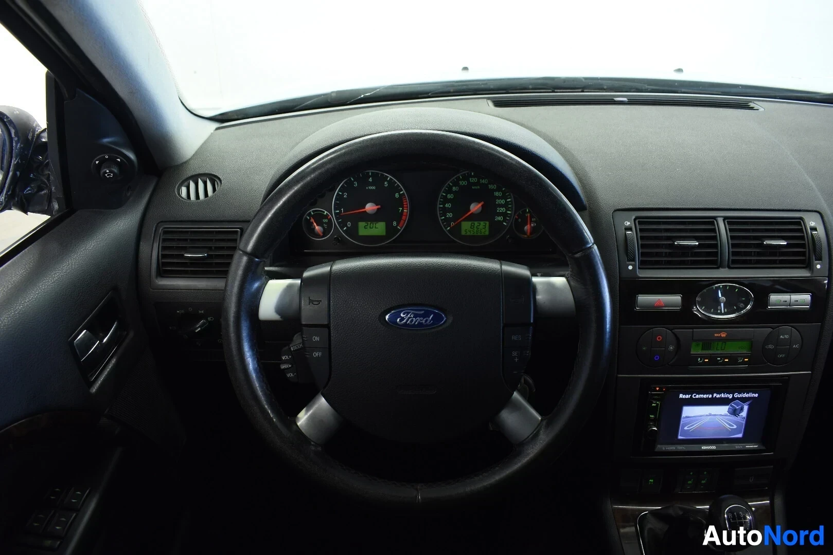 Ohjaamo: Kuvassa näkyy auton ohjauspyörä ja osa kojelautaa. Ohjauspyörässä on Ford-logo ja monitoimipainikkeet. Mittaristo näyttää lukemia, vasemmassa mittarissa luku 20