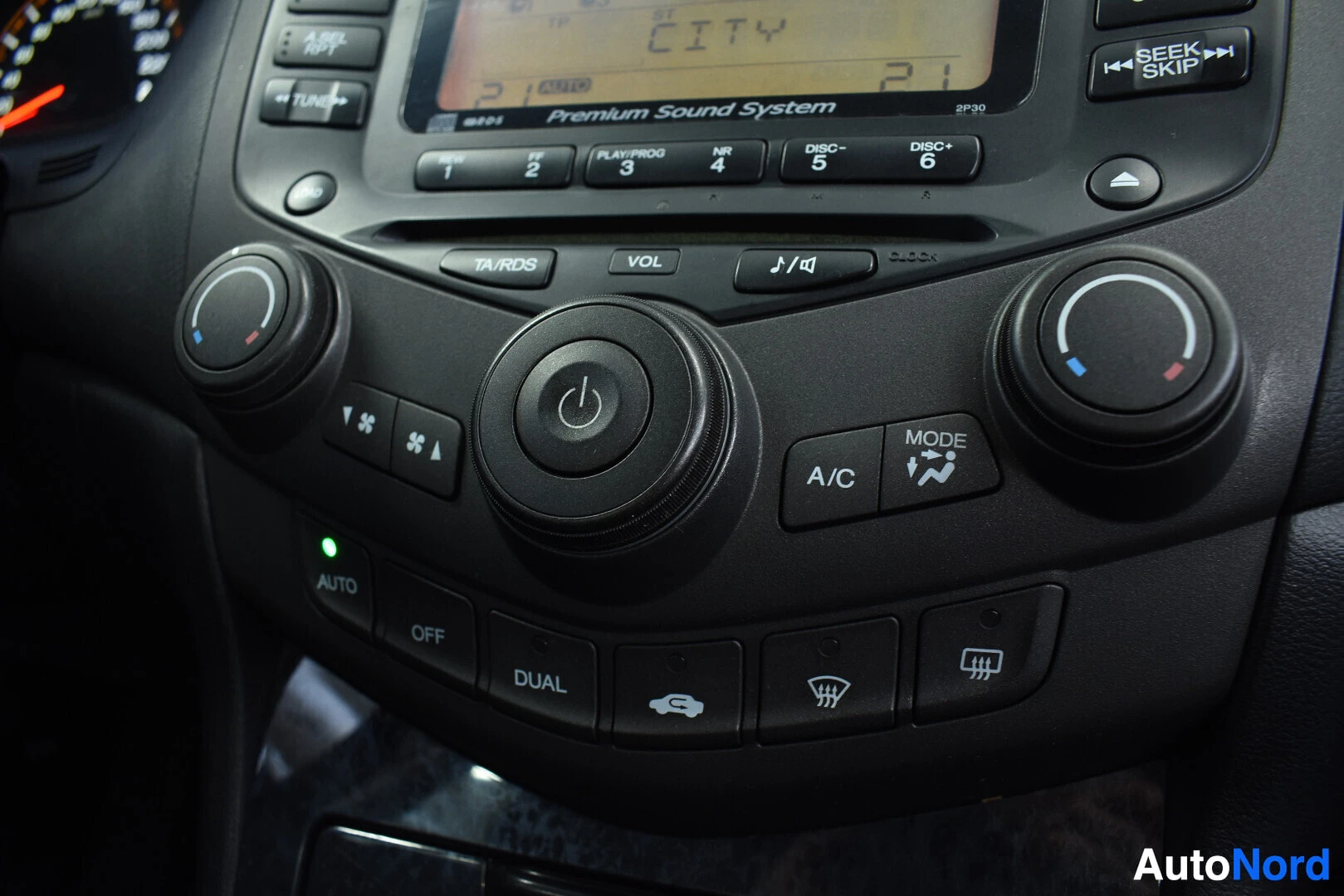 Yksityiskohta: Lähikuva auton ilmastointi- ja radion säätimistä keskikonsolissa. Painikkeet "A/C", "AUTO" ja "DUAL" ovat näkyvissä.