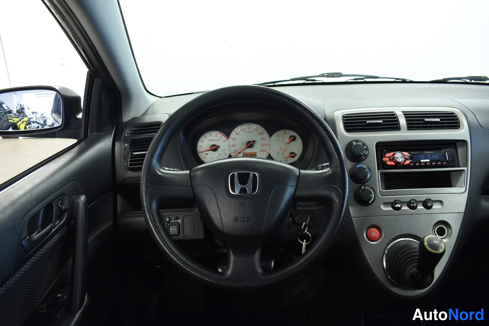 Muu: Honda Civicia ohjaamosta: ohjauspyörä, mittaristo, radioteline ja käsivaihteisto näkyvät etupenkiltä kuvattuna.