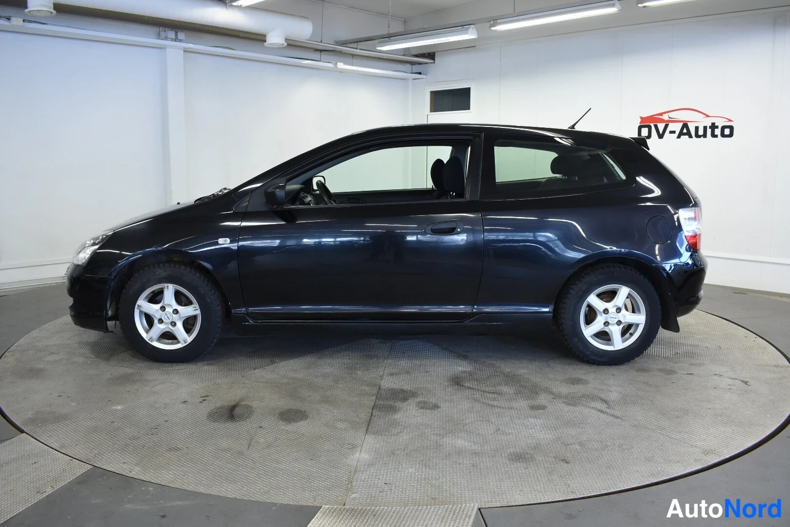 Sivulta: Mustan Honda Civigin sivunäkymä vasemmalta, kaksiovinen hatchback, hopeavanteiset pyörät ja ovipeilit näkyvät.