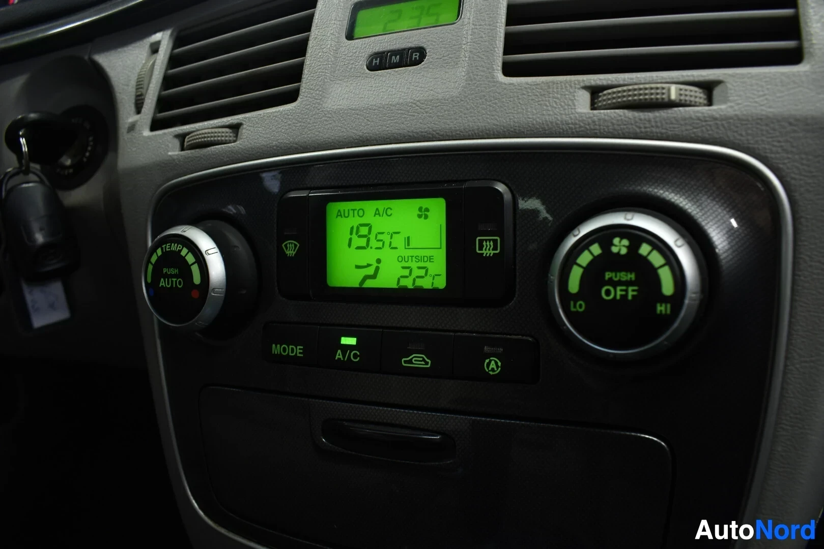 Yksityiskohta: Lähikuva auton ilmastoinnin säätimistä ja näytöstä, jossa näkyy teksti 'AUTO A/C' ja lämpötilat 19.5 C ja 22 C.