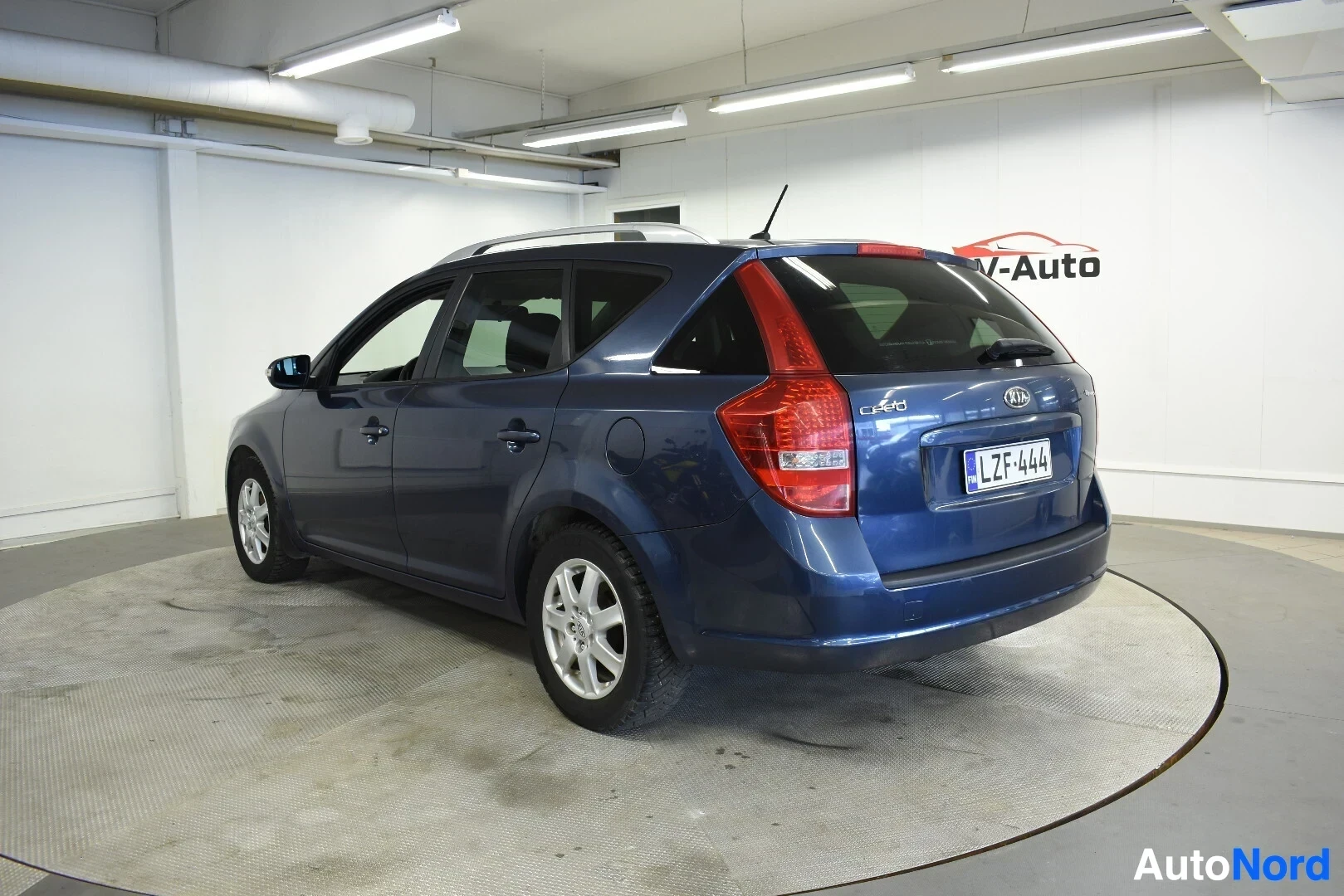Takaviisto: Sininen farmariauto takaviistosta oikealta kuvattuna kääntöalustalla sisätiloissa.