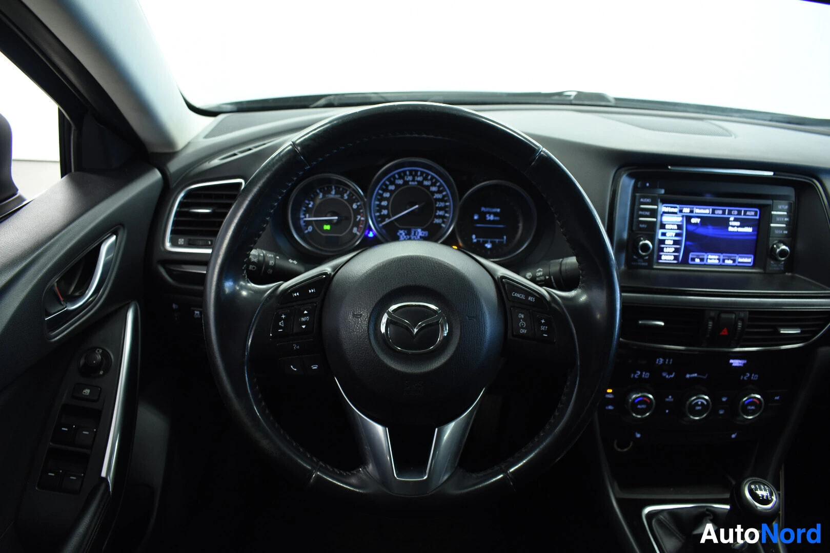 Yksityiskohta: Lähikuva ohjauspyörästä, jossa on Mazda-logo ja monitoimipainikkeita. Mittaristo näkyy ohjauspyörän takana.