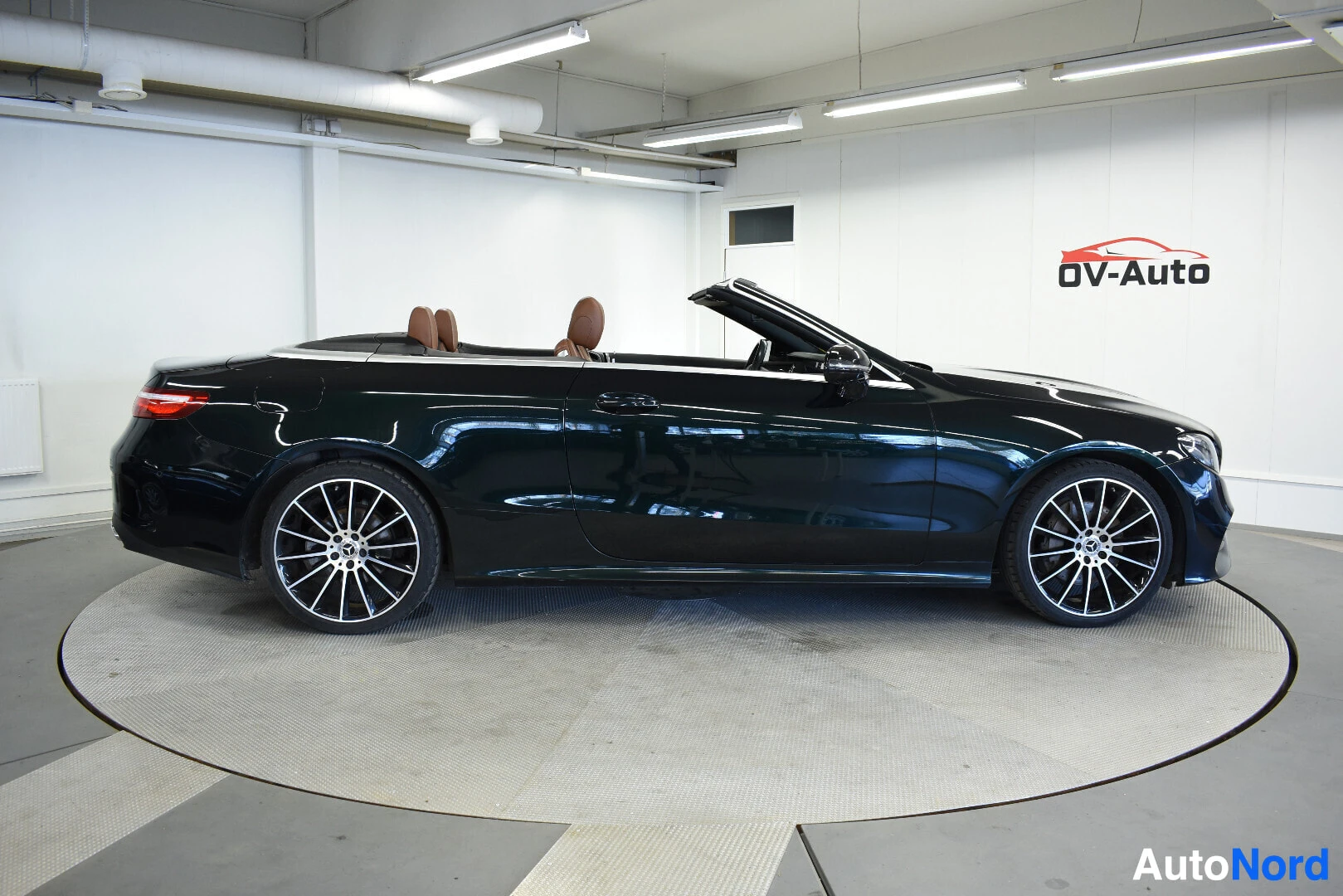 Sivulta: Tummanvihreä Mercedes-Benz avoauto vasemmalta sivulta kuvattuna, katto alhaalla. Autossa on monipuoliset kevytmetallivanteet.