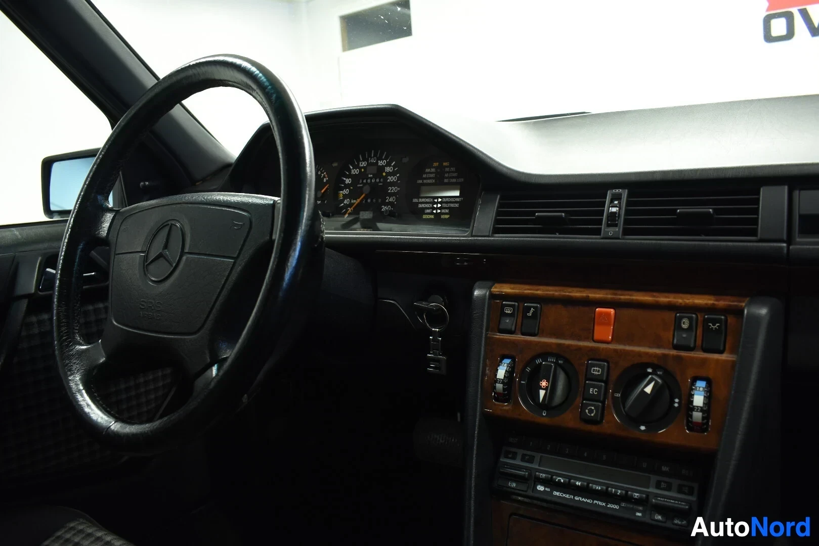 Ohjaamo: Ohjauspyörä, jossa on Mercedes-Benz-logo, mittaristo, kojelauta, tuuletusaukot ja puujäljitelmäverhoiltu keskikonsoli, jossa on säätimet ja autoradio.