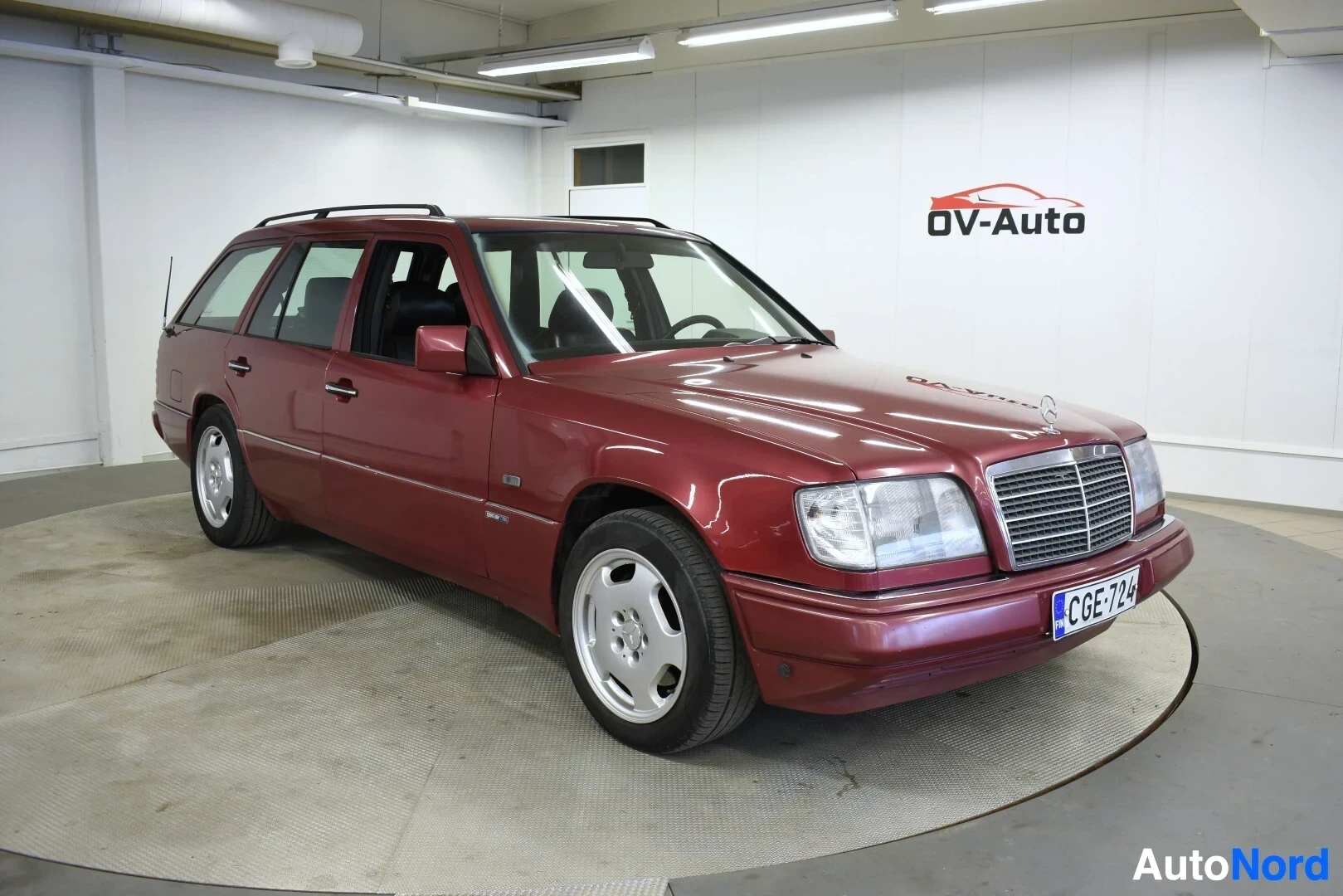 Etuviisto, nokka oikealle: Mercedes-Benz E 320 -farmari punaisena sisätiloissa, etukulmanäkymä, rekisterikilpi.