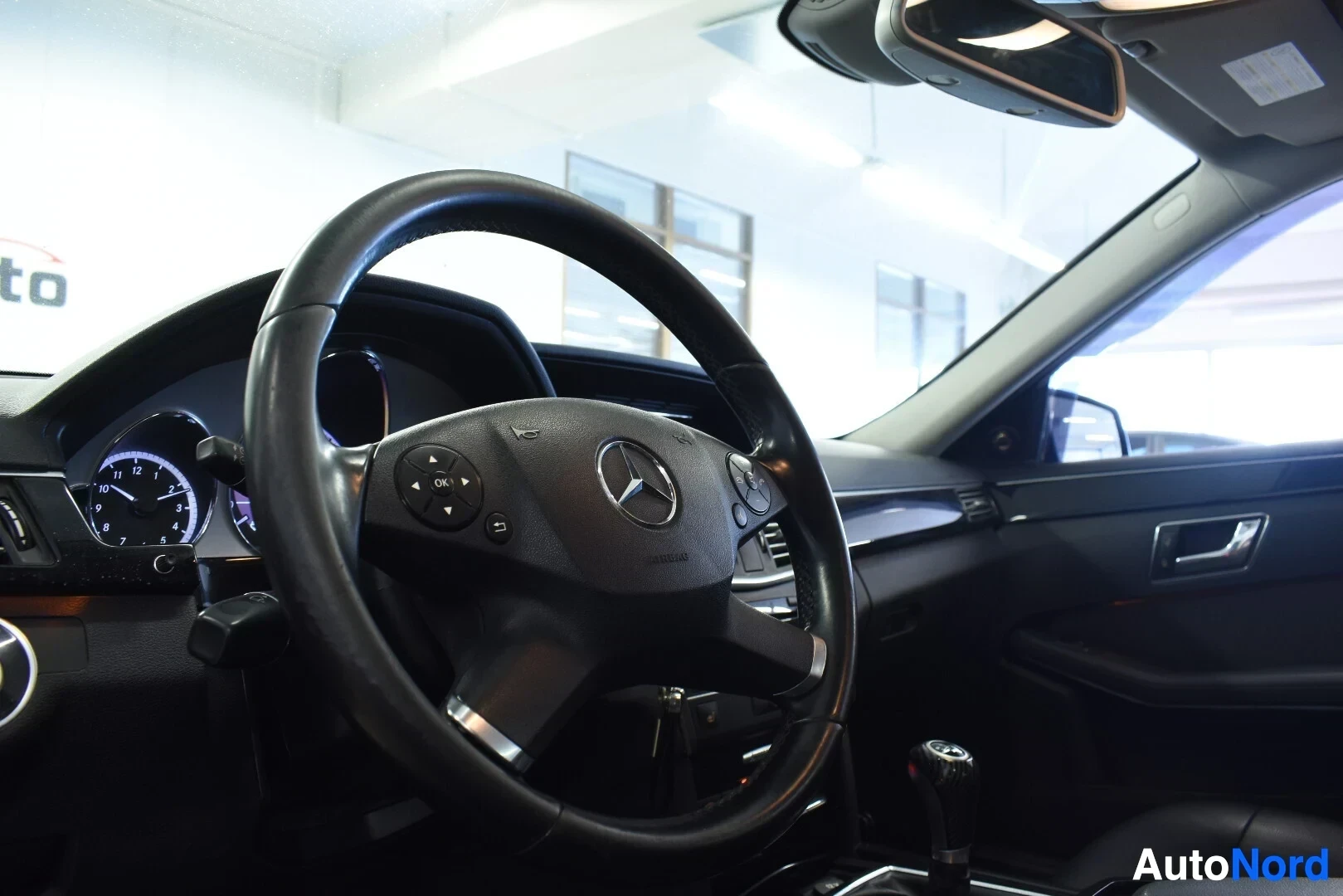 Ohjaamo: Ohjauspyörä, jossa on Mercedes-Benz-logo ja monitoimiohjaimen painikkeet vasemmalla puolella. Mittaristo näkyy ohjauspyörän takana vasemmalla.
