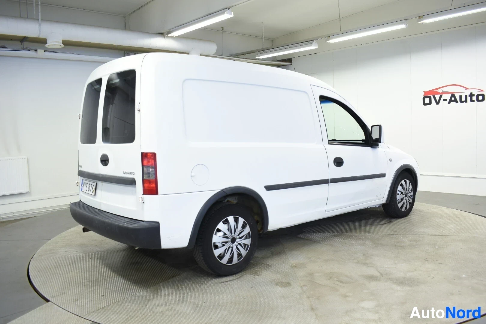 Takaviisto: Valkoinen pakettiauto kuvattuna takaoikealta. Mustat pölykapselit näkyvät renkaissa.