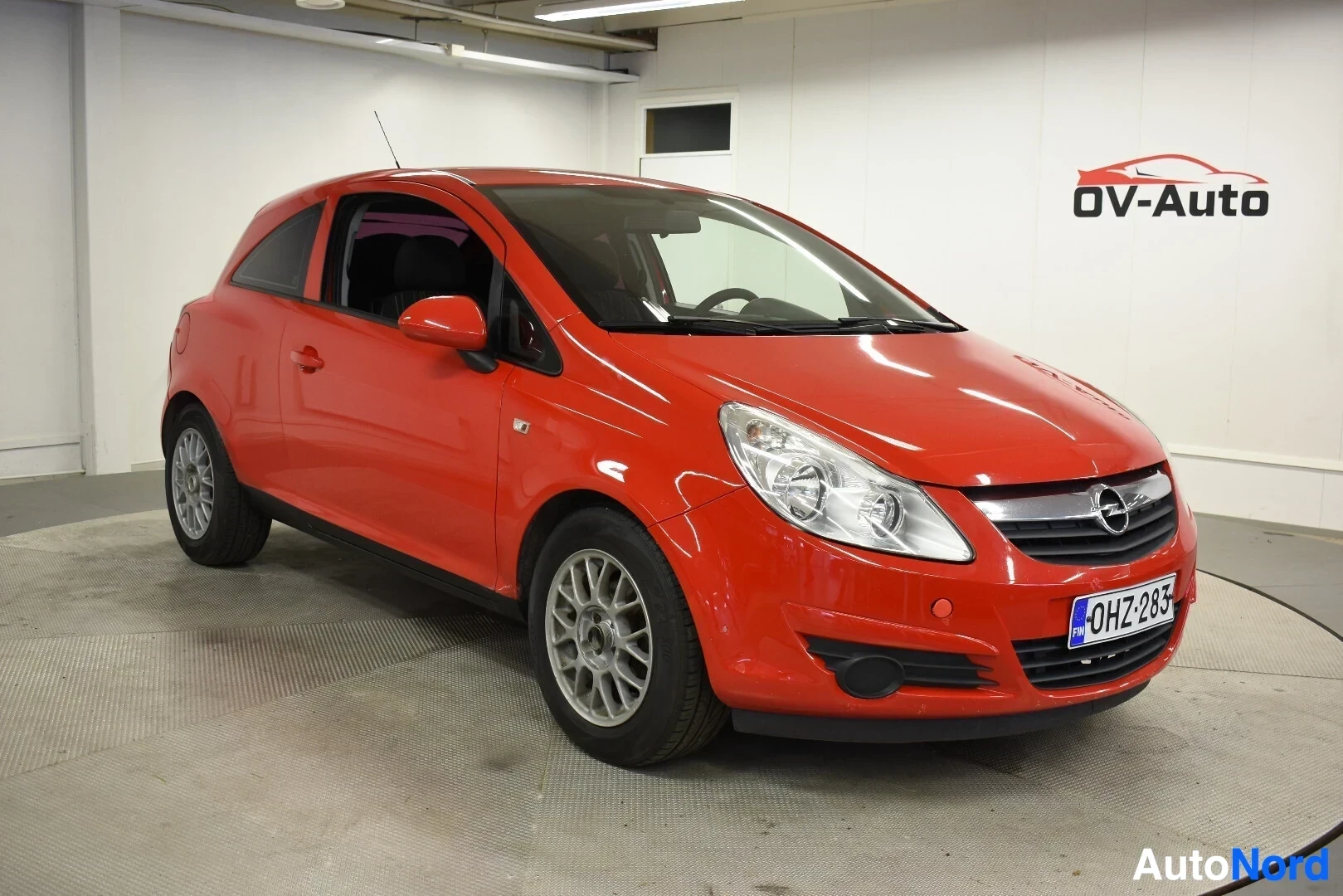 Etuviisto, nokka oikealle: Punainen Opel Corsa edestä ja oikealta sivulta kuvattuna. Autossa on hopeanväriset vanteet ja rekisterikilpi