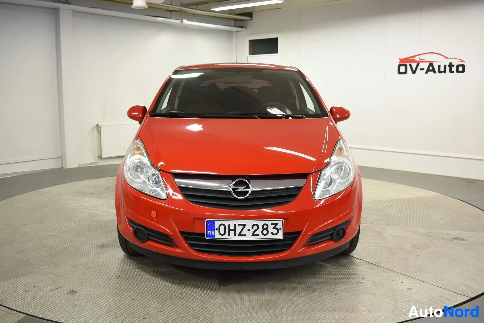 Edestä: Punainen Opel Corsa kuvattuna suoraan edestä. Autossa on rekisterikilpi
