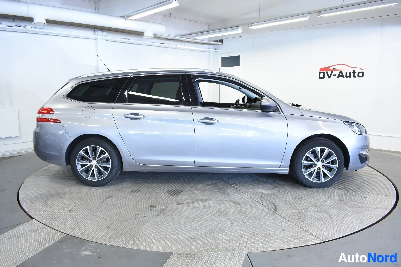 Sivulta: Hopeanvärinen Peugeot 308 SW vasemmalta sivulta kuvattuna. Ajoneuvossa on kattokiskot.