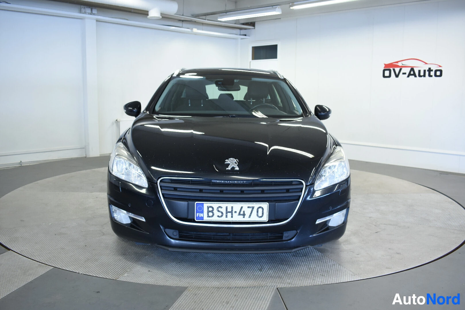Edestä: Musta Peugeot 508 SW farmariauto edestä päin kuvattuna, rekisterikilpi näkyvissä. Auto on valkoisessa hallissa pyörivällä alustalla