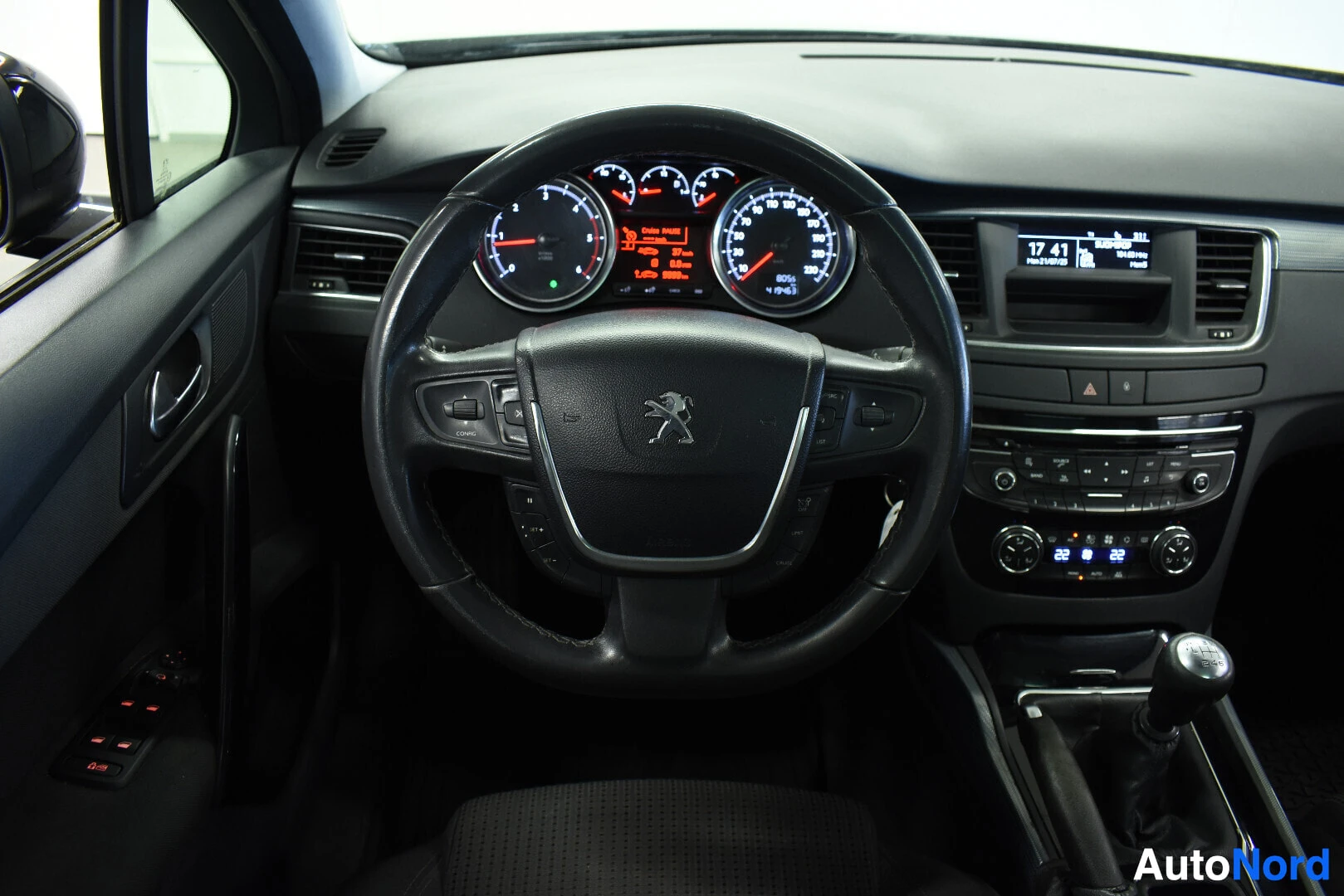 Ohjaamo: Lähikuva auton ohjauspyörästä ja mittaristosta. Ohjauspyörässä on Peugeot-logo ja monitoimipainikkeet. Mittaristo näyttää kierrosluvun ja nopeuden. Keskikonsoli