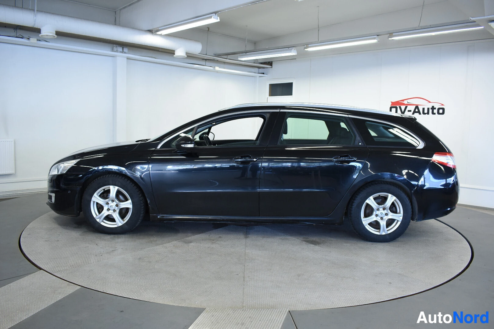 Sivulta: Musta Peugeot 508 SW farmariauto oikealta kyljeltä kuvattuna. Auto on valkoisessa hallissa pyörivällä alustalla.