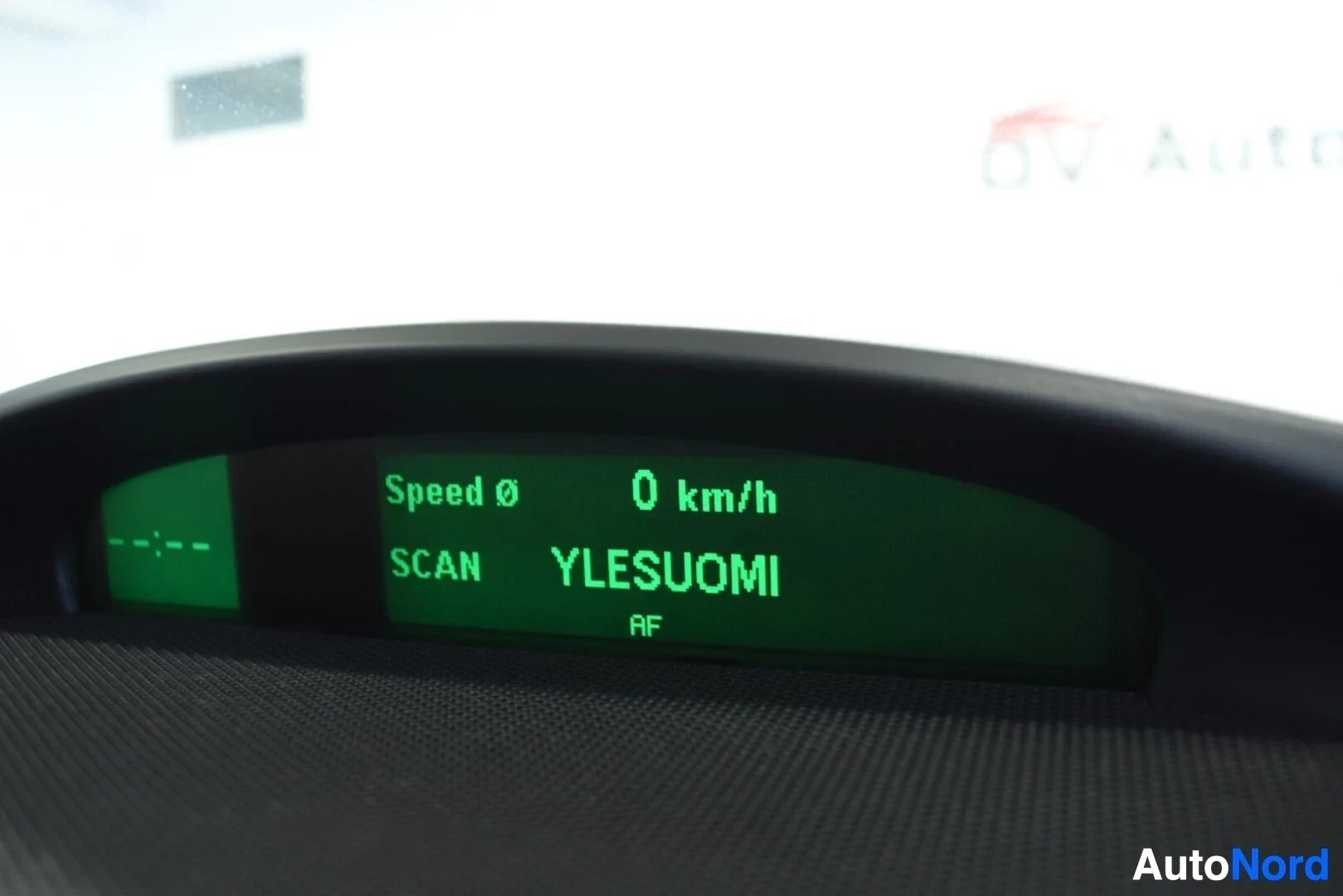 Yksityiskohta: Lähikuva kojelaudan näytöstä, jossa näkyy teksti "Speed 0 0 km/h" ja "SCAN YLEISUOMI AF".