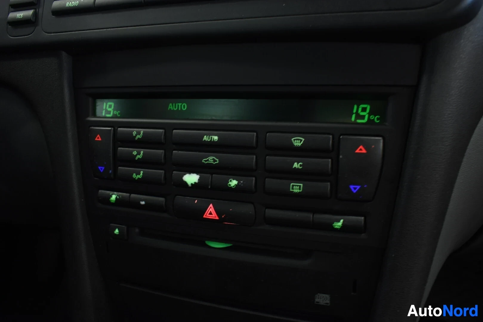 Yksityiskohta: Kuva auton keskikonsolin ilmastointipaneelista, jossa näkyy digitaalinen näyttö "19ºC AUTO 19ºC" sekä useita painikkeita, kuten "AC" ja lämmitettävien istuimien