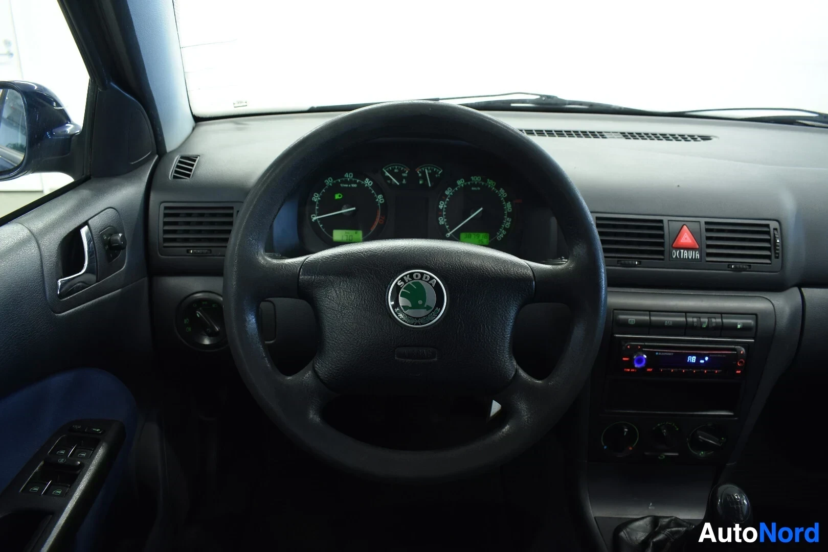 Yksityiskohta: Kuvakulma näyttää auton ohjauspyörän ja mittariston yksityiskohdan. Mittaristo näyttää kierrosluvun ja nopeuden. Ohjauspyörän keskiössä on Skoda-logo ja airbag-