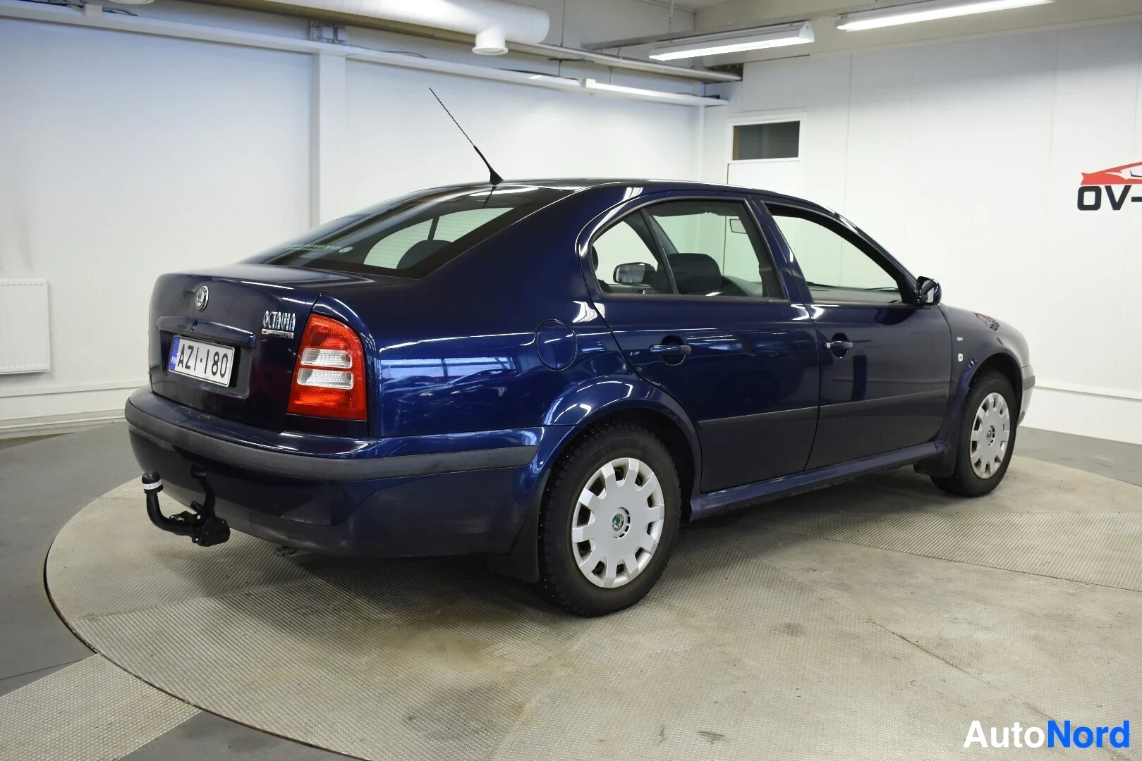 Takaviisto: Tummanpunainen Skoda Octavia -henkilöauto, jossa on vetokoukku, kuvattuna taka-vasemmalta viistosta.