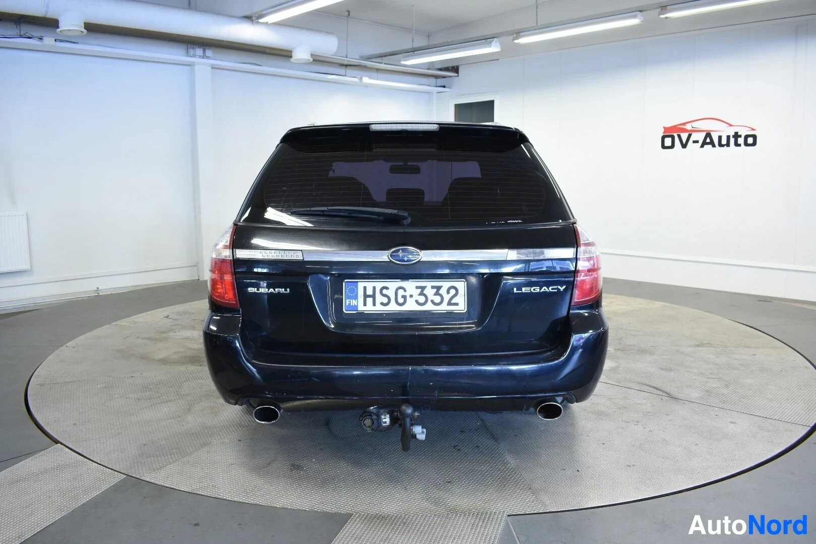 Takaa: Mustan farmariauton takaosa, jossa näkyvät takavalot, takaluukku ja rekisterikilpi H-S-G-332. Autossa on vetokoukku.