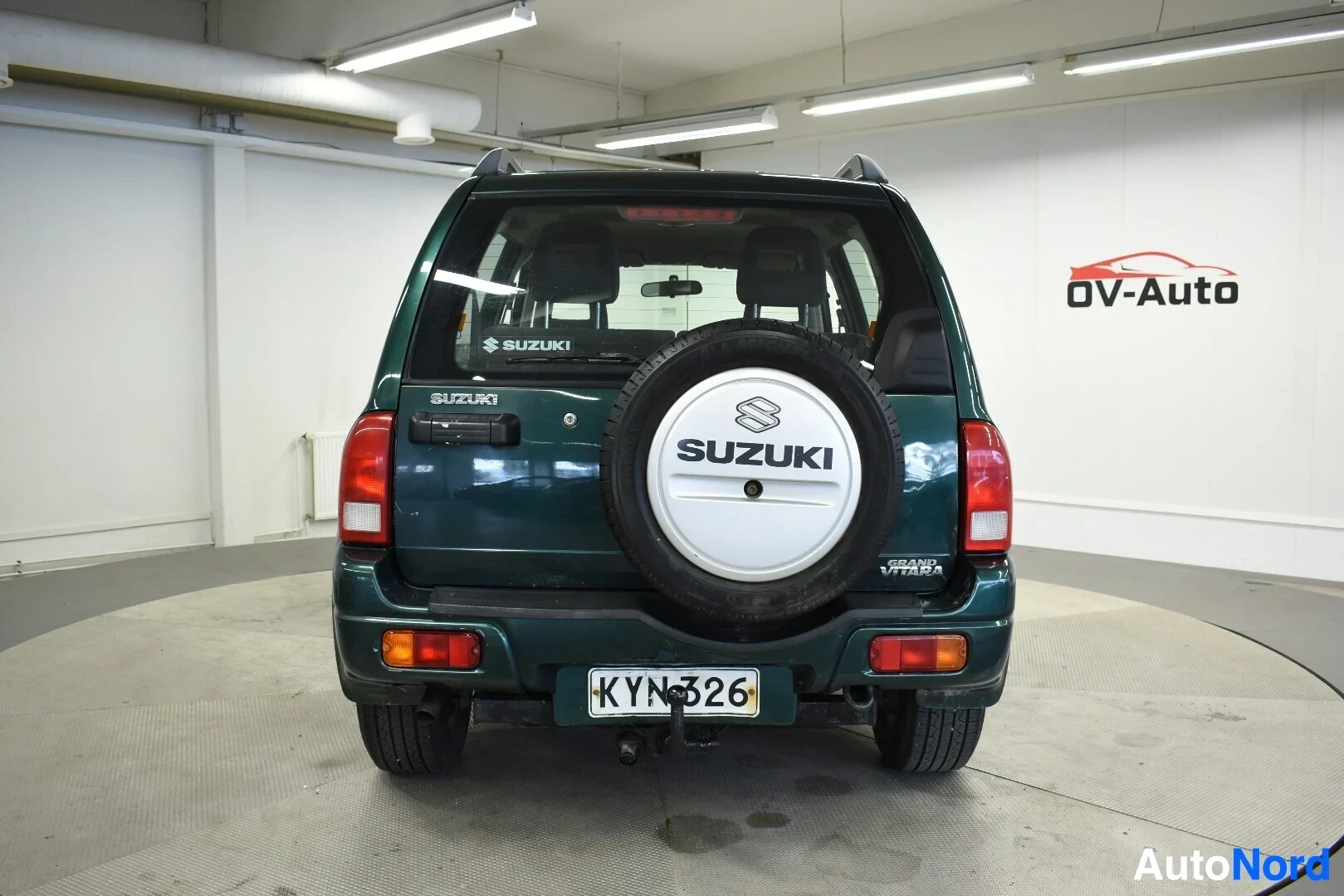 Takaa: Tummanvihreä maastoauto, jossa on vararengas takaluukussa ja vetokoukku, kuvattuna suoraan takaa.