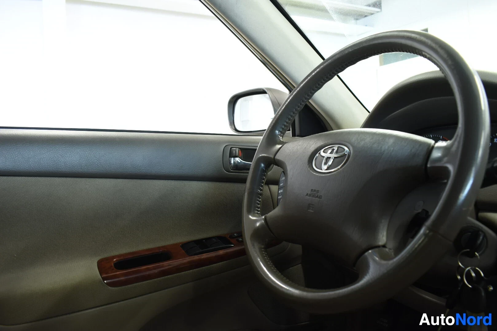 Ohjaamo: Ohjauspyörä Toyota-logolla ja kuljettajan oven sisäpaneeli, jossa ikkunannostimien katkaisijat ja puujäljitelmäverhoilu.