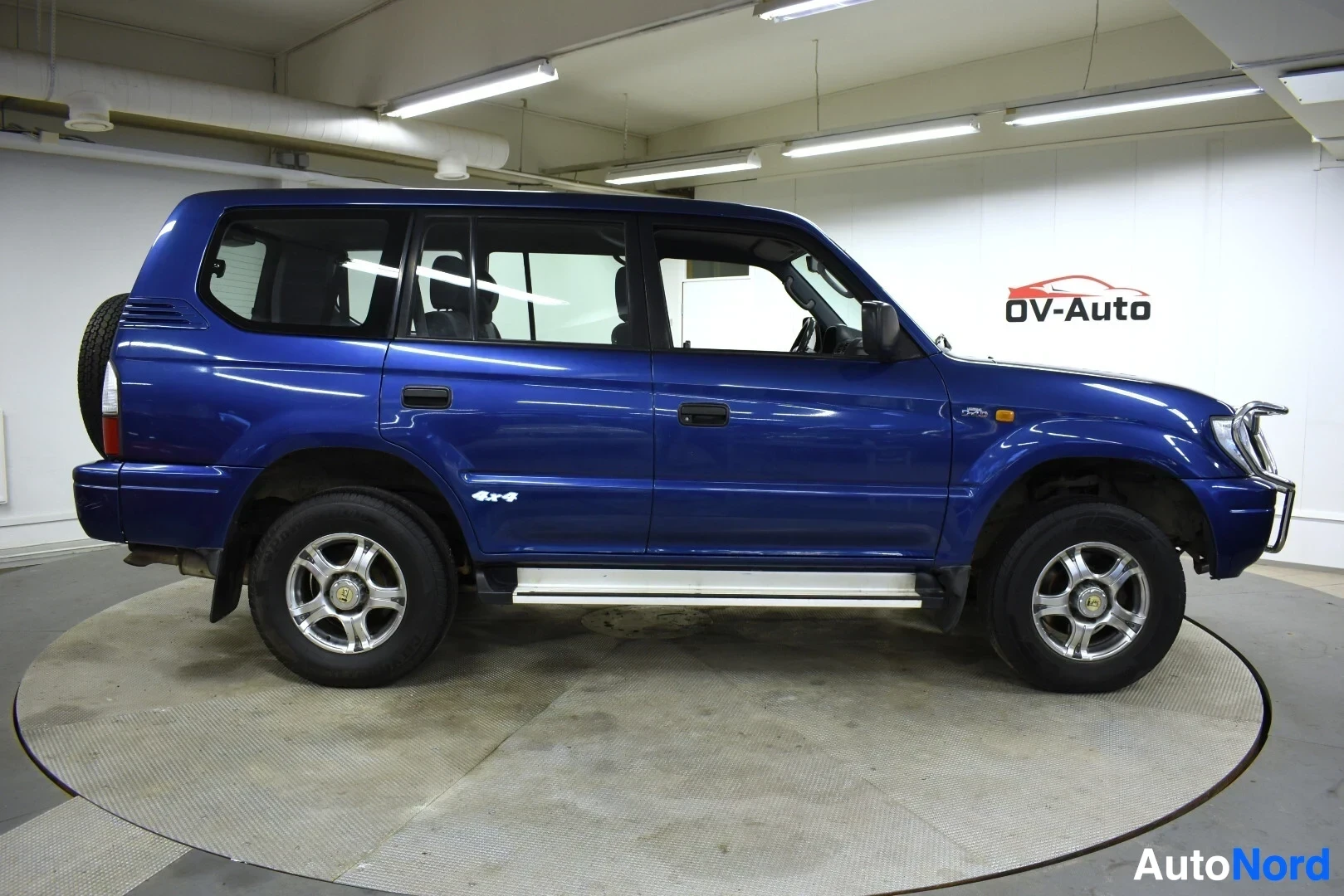 Sivulta: Tummansininen maastoauto kuvattuna sivulta oikealta. Autossa on astinlaudat ja kevytmetallivanteet. Auton kyljessä on "4x4"-tarra.