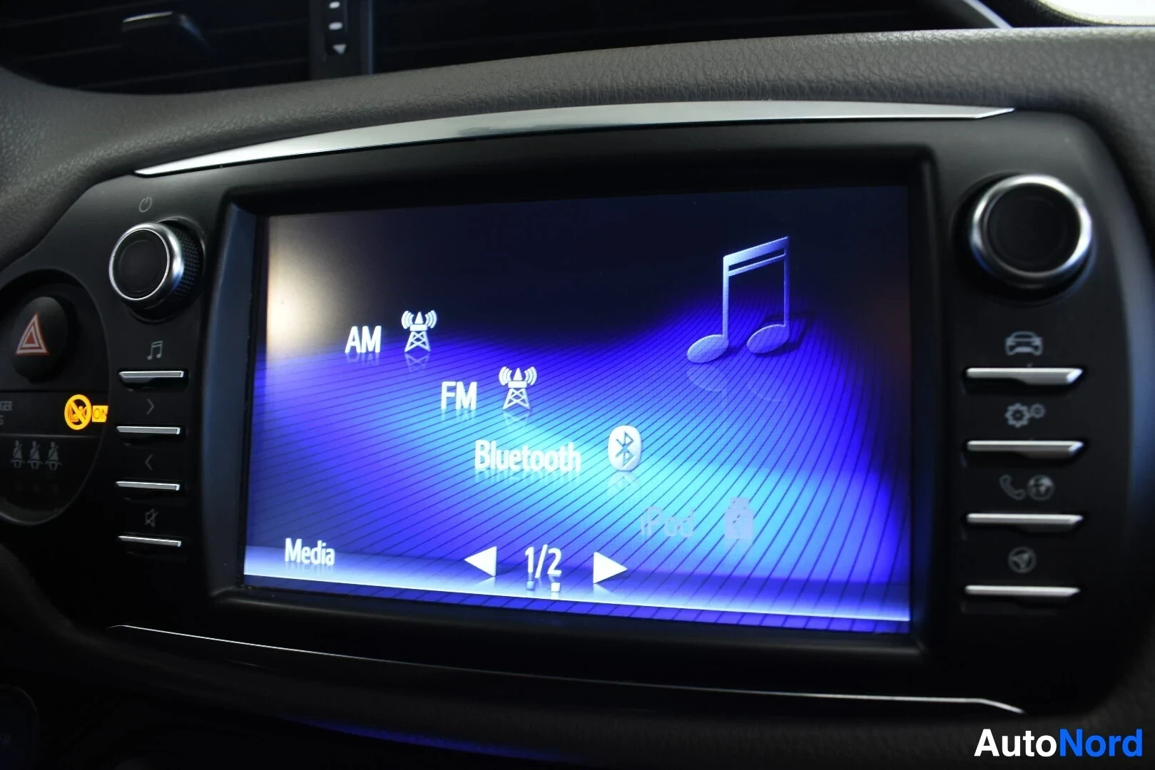 Yksityiskohta: Lähikuva auton tietoviihdejärjestelmän kosketusnäytöstä. Näytöllä näkyvät vaihtoehdot AM, FM ja Bluetooth, joissa on vastaavat kuvakkeet.
