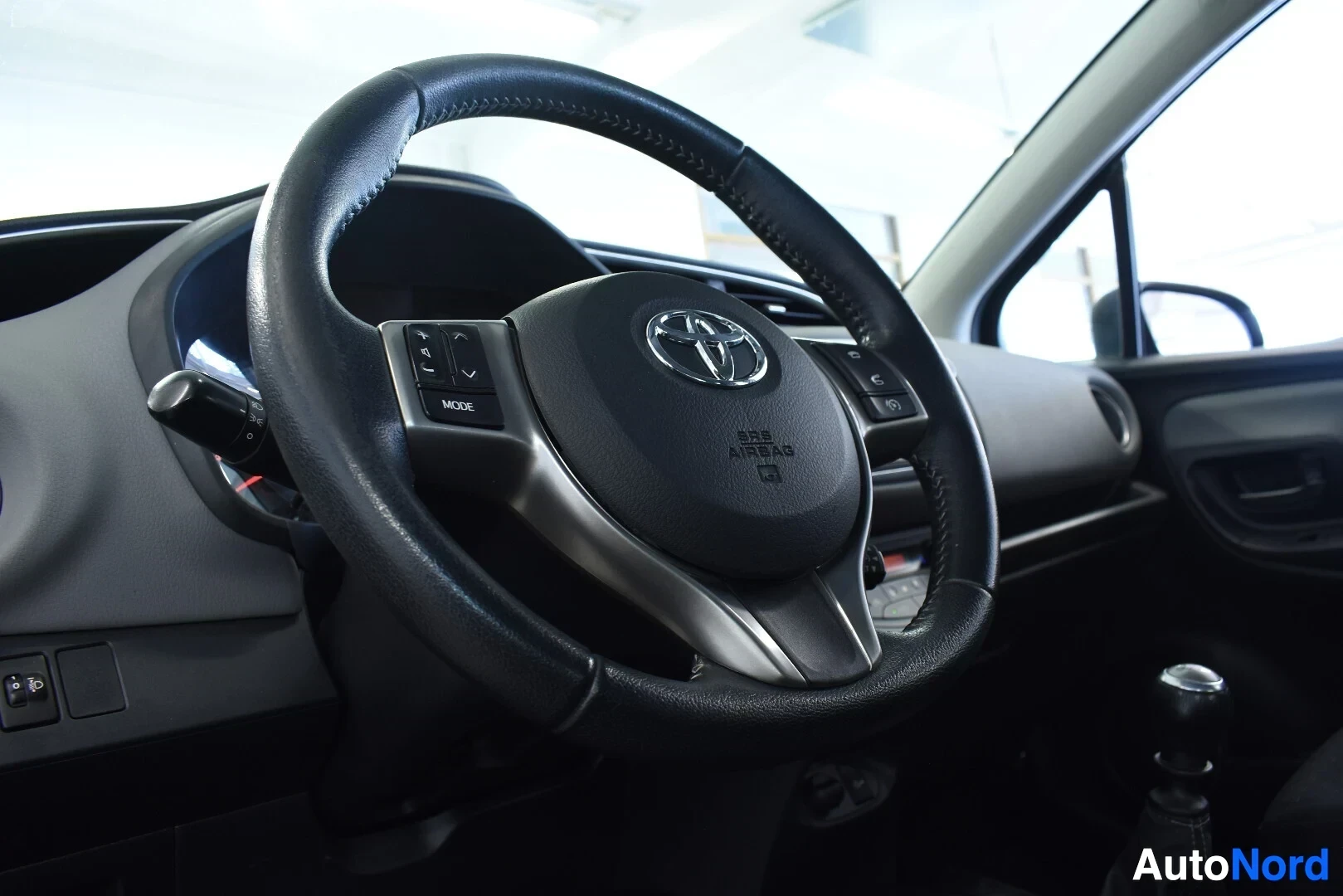 Ohjaamo: Ohjauspyörä ja osa kojelautaa matkustajan puolelta kuvattuna. Ratissa on Toyota-logo ja teksti 'SRS AIRBAG'.