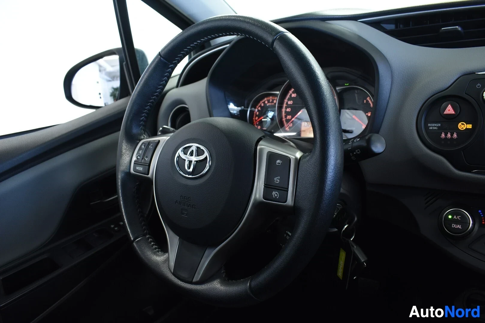 Ohjaamo: Ohjauspyörä ja kojelauta. Ratissa on Toyota-logo ja monitoiminäppäimet. Kojelaudassa näkyy varoitusvaloja ja avaimet roikkuvat virtalukossa.