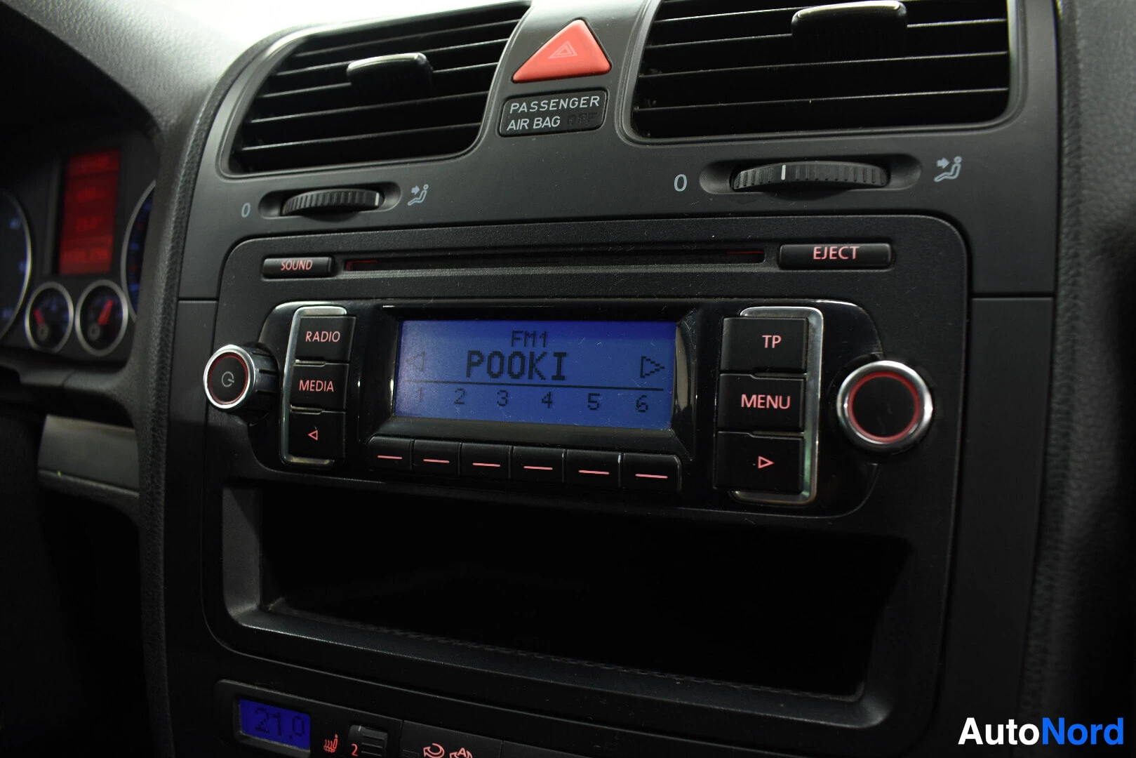 Yksityiskohta: Lähikuva auton keskikonsolista, jossa näkyy radio ja ilmastoinnin säätimet. Radion näytössä lukee "FM1 POOKI" ja sen alla on numerot 1-6. Radion ympärillä on pa