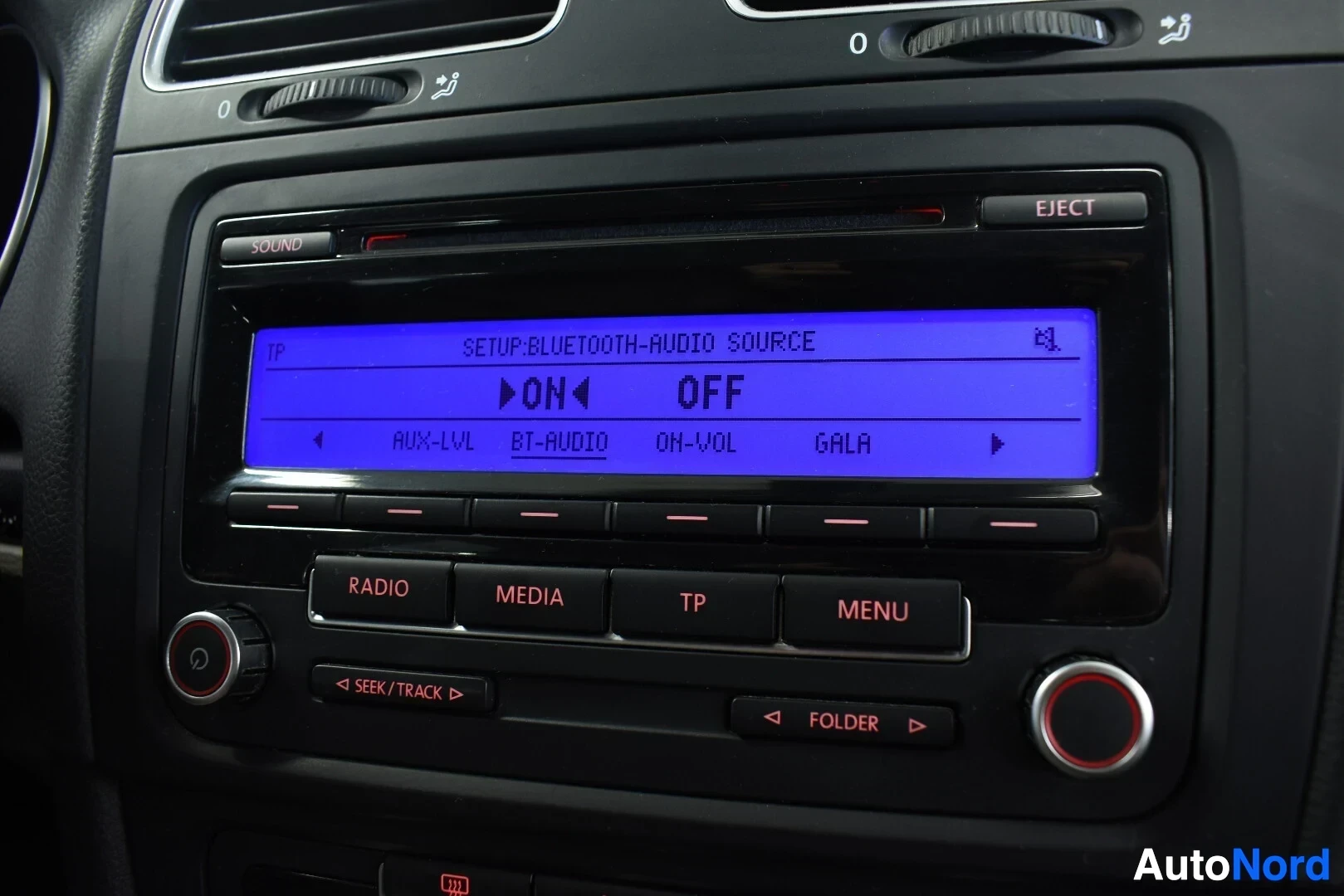 Yksityiskohta: Lähikuva auton keskinäytöstä, jossa sinisellä taustalla lukee "SETUP-BLUETOOTH-AUDIO SOURCE" ja "ON ▶ OFF".