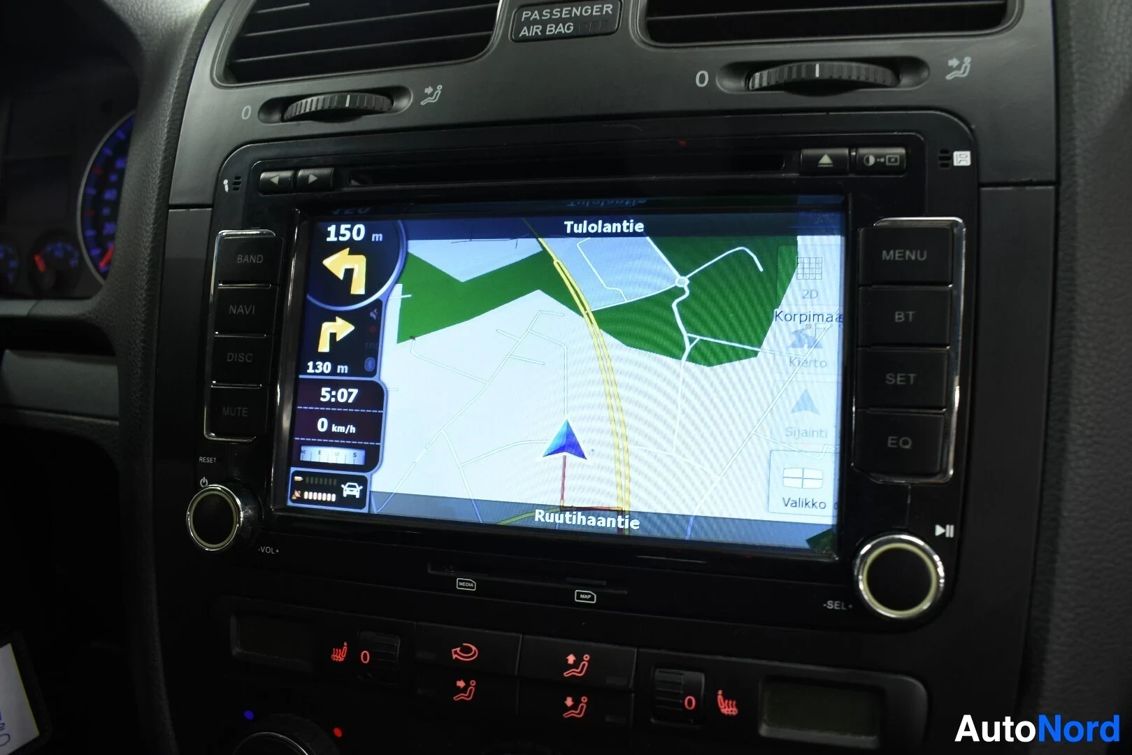 Ohjaamo: Lähikuva auton infotainment-näytöstä, jossa näkyy navigointiohjelma karttanäkymällä. Näytöllä on osoite "Tulolantie" ja reittiohjeet, jotka ilmoittavat 150 metr