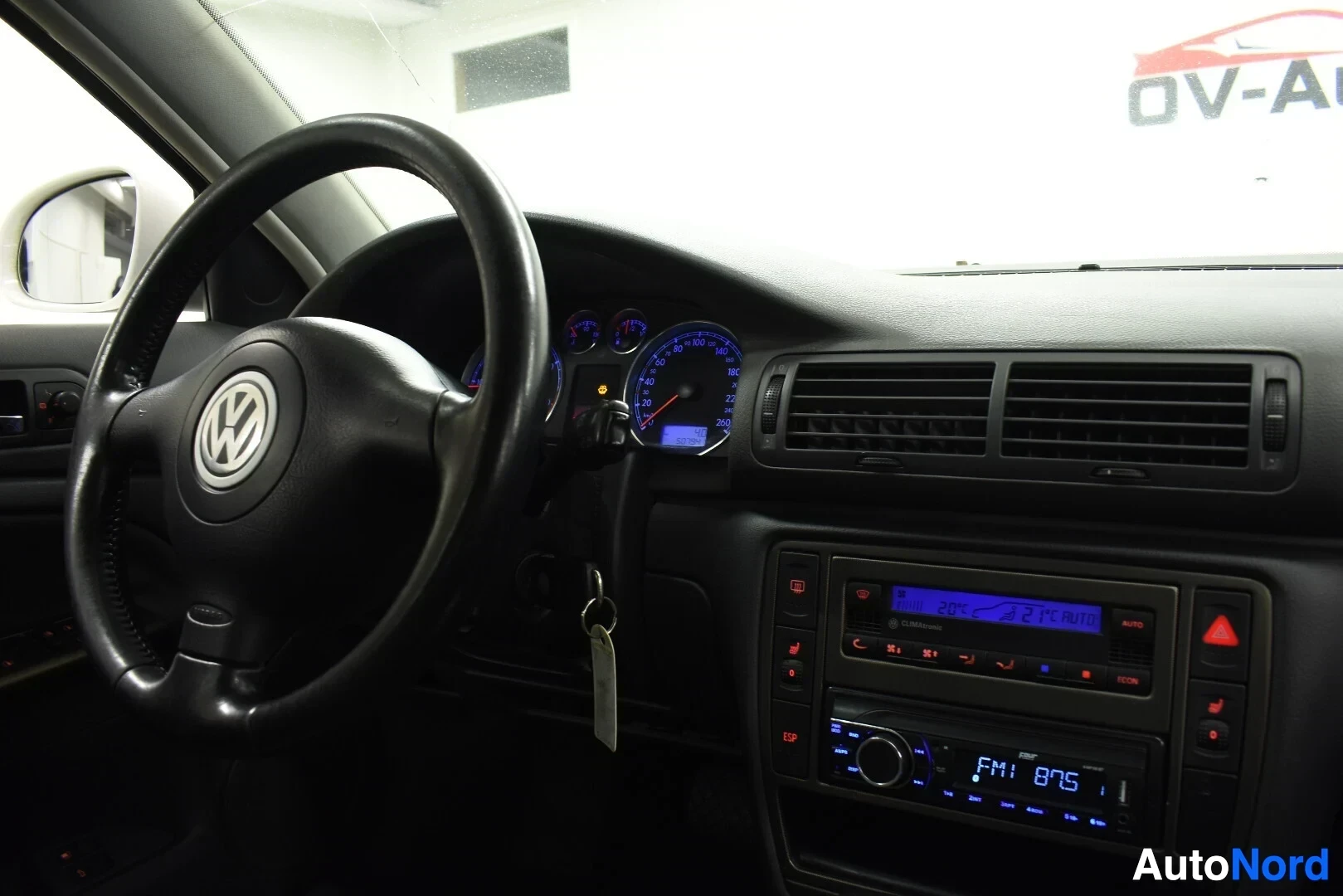 Yksityiskohta: Kuvassa auton ohjaamo oikealta, ohjauspyörä on vasemmalla ja keskikonsolin radio näkyy. Radiossa lukee "FM1 87.5" ja "22°C AUTO".