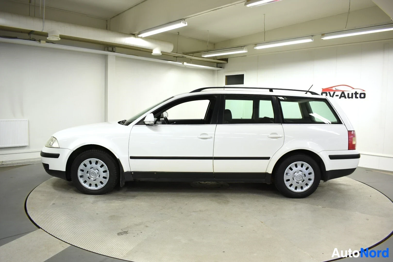 Sivulta: Valkoinen farmariauto oikealta sivulta katsottuna, katolla kattokiskot. Autossa peltivanteet.