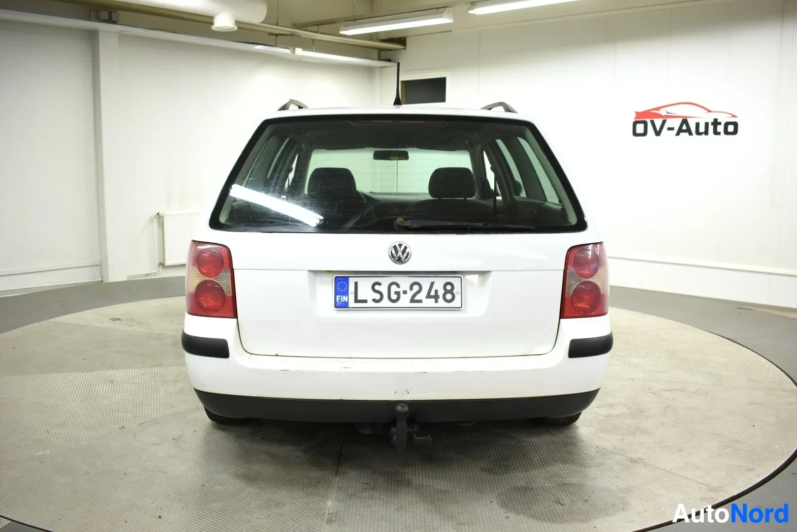 Takaa: Valkoinen farmariauto, jossa on mustat kattokaiteet ja vetokoukku, takaapäin kuvattuna.