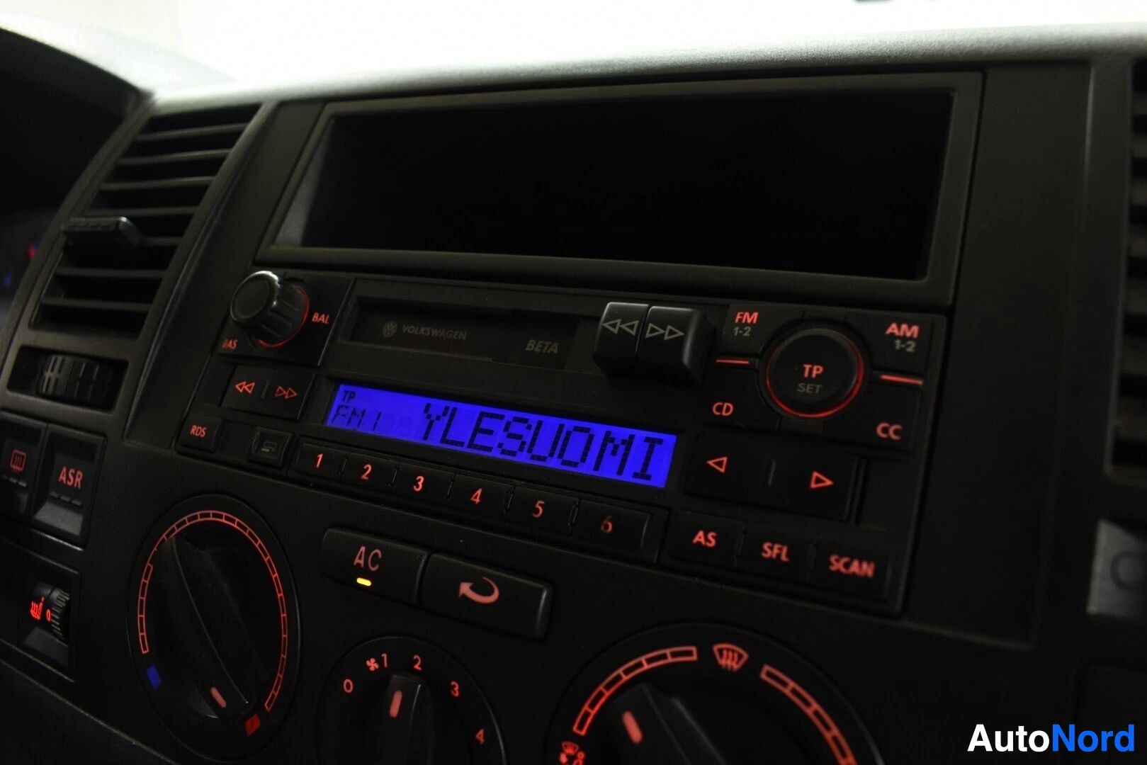 Yksityiskohta: Volkswagenin radiolaite, jonka näytöllä lukee "FM 1 YLEISUOMI" ja alapuolella ohjauspaneeli, jossa on painikkeita ja kolme pyöreää säädintä.