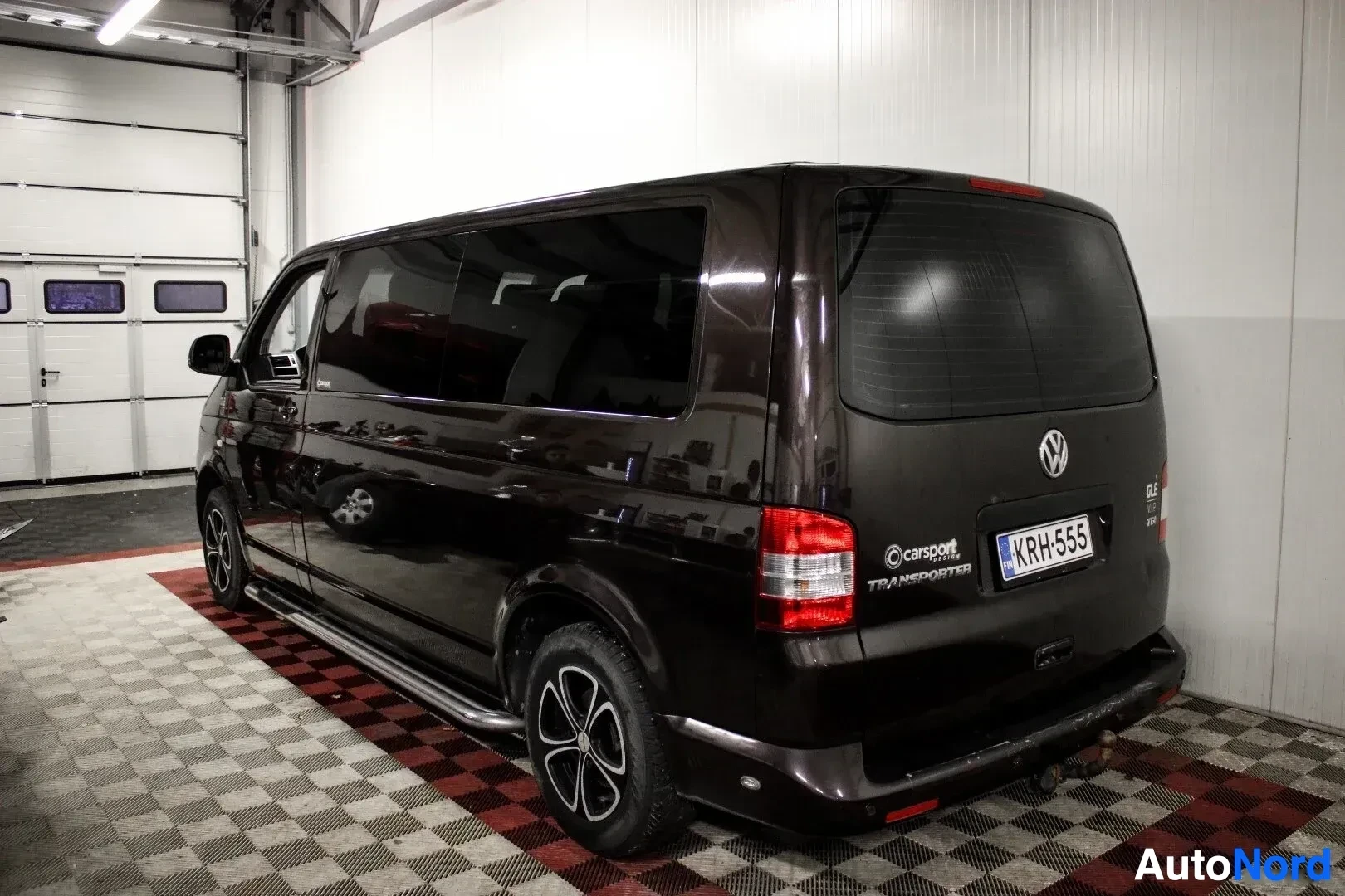Takaviisto: Tummanruskean pakettiauton takaosa ja oikea kylki kuvattuna viistosti takaa oikealta. Ajoneuvossa on vetokoukku, astinlaudat ja takana tekstit "Carsport Design"