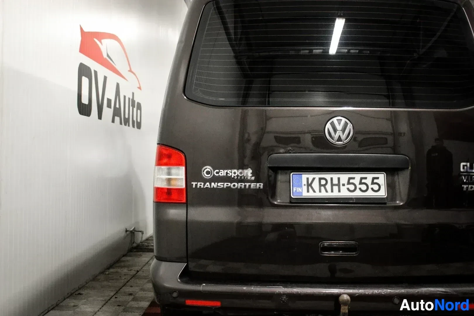 Takaa: Yksityiskohtakuva pakettiauton takaosasta, jossa näkyvät takaluukun merkinnät "Carsport Design", "Transporter", "GTE", "VIP", "TDI" ja rekisterikilpi "KR-H 555"