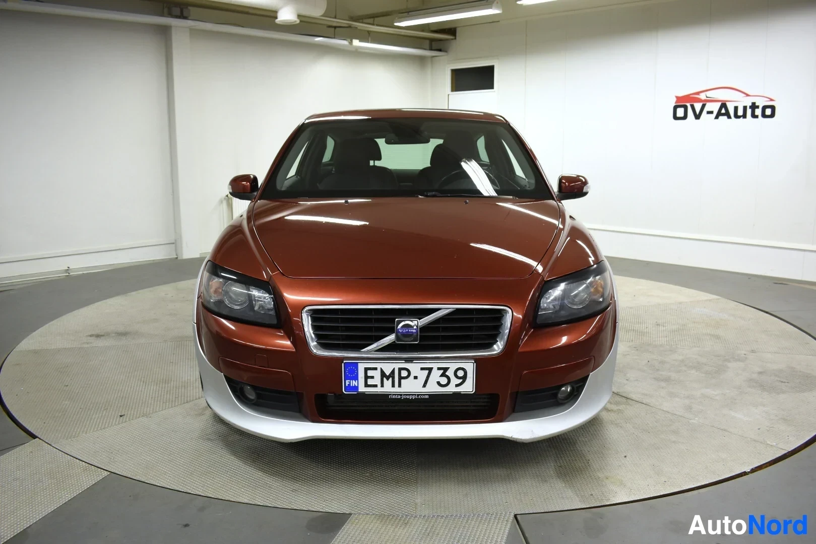 Edestä: Oranssinruskea Volvo C30 edestäpäin kuvattuna. Autossa on vaaleanharmaat alahelmat edessä. Rekisterikilpi näkyvissä