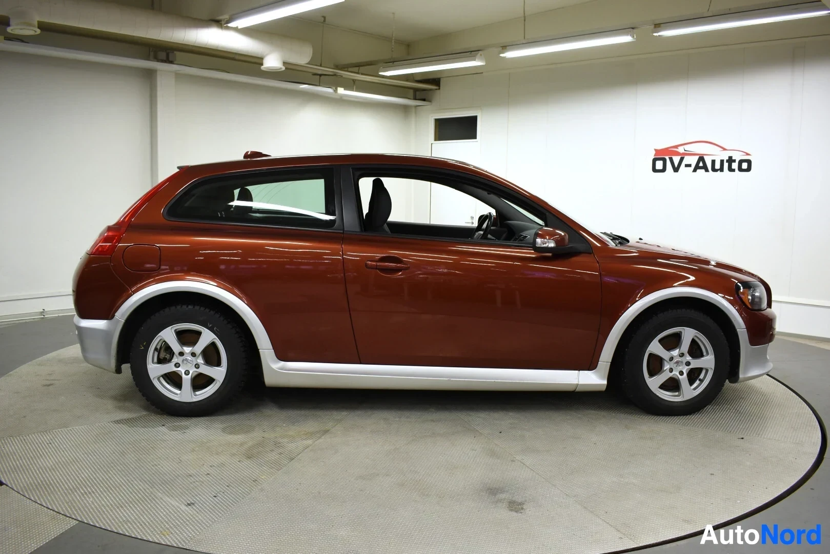 Sivulta: Volvo C30 -henkilöauto kuvattuna oikealta sivulta. Autossa on ruskea kori ja harmaat helmat. Oikeassa etuovessa on musta suojalista. Autossa on viisipuolaiset k