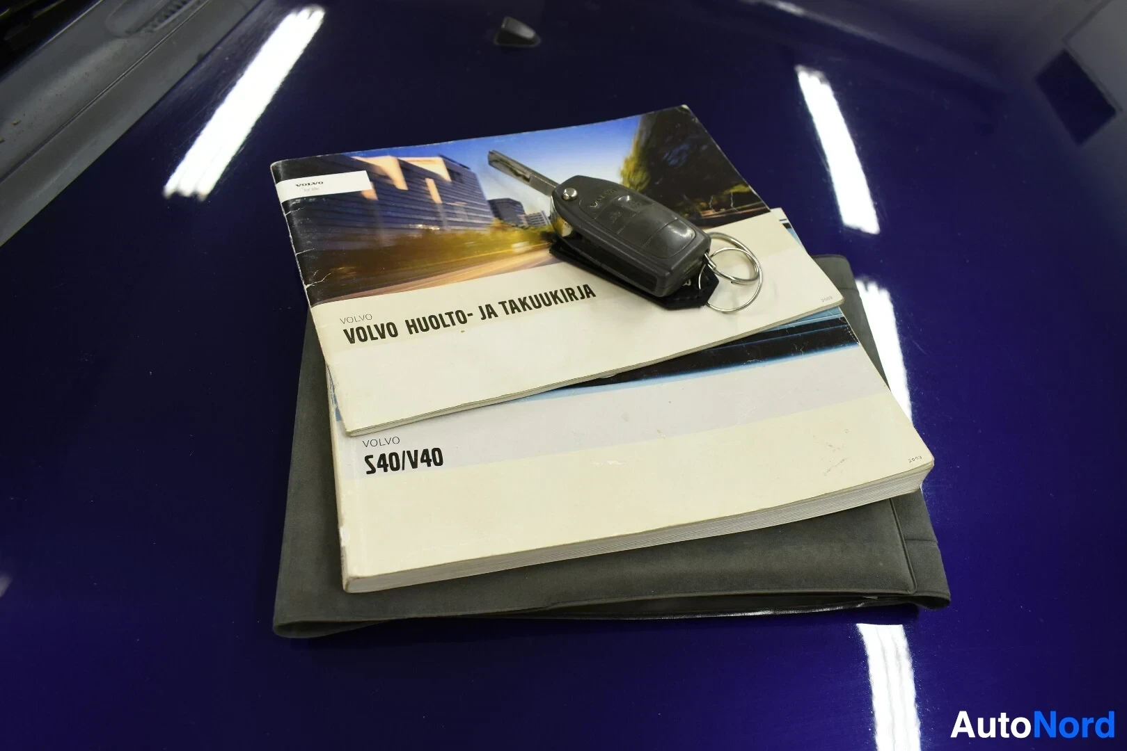 Asiakirja: Lähikuva avaimesta ja kahdesta Volvo-ohjekirjasta, joiden kannessa lukee "VOLVO HUOLTO- JA TAKUUKIRJA" ja "VOLVO S40/V40".
