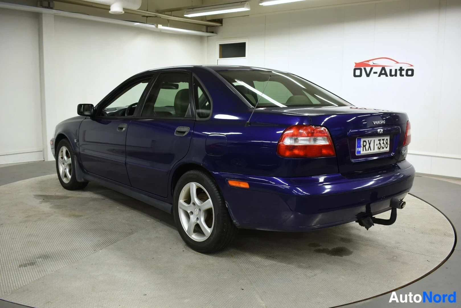 Takaviisto: Sininen sedan-tyyppinen henkilöauto kuvattuna takaviistosta oikealta puolelta, jossa näkyy perä ja oikea kylki. Autossa on vetokoukku.