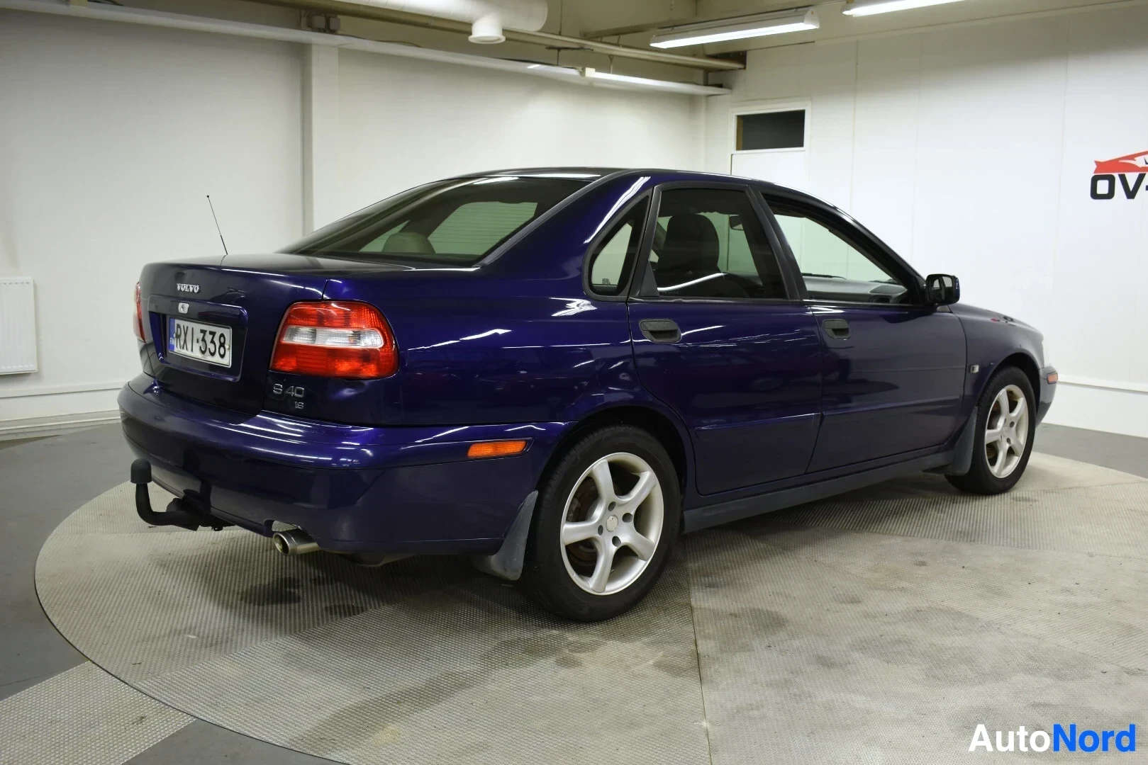 Takaviisto: Sininen sedan-tyyppinen henkilöauto kuvattuna takaviistosta vasemmalta puolelta, jossa näkyy perä ja vasen kylki. Autossa on vetokoukku.