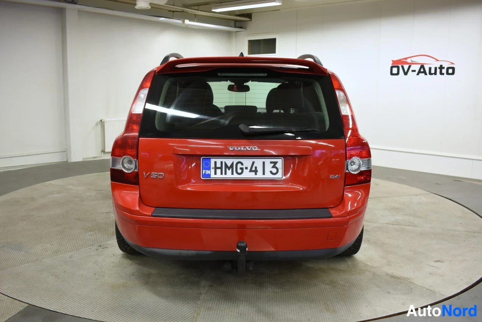Takaa: Oranssinpunainen Volvo V50 farmariauto takaa päin kuvattuna. Autossa on vetokoukku. Rekisterikilpi on näkyvillä