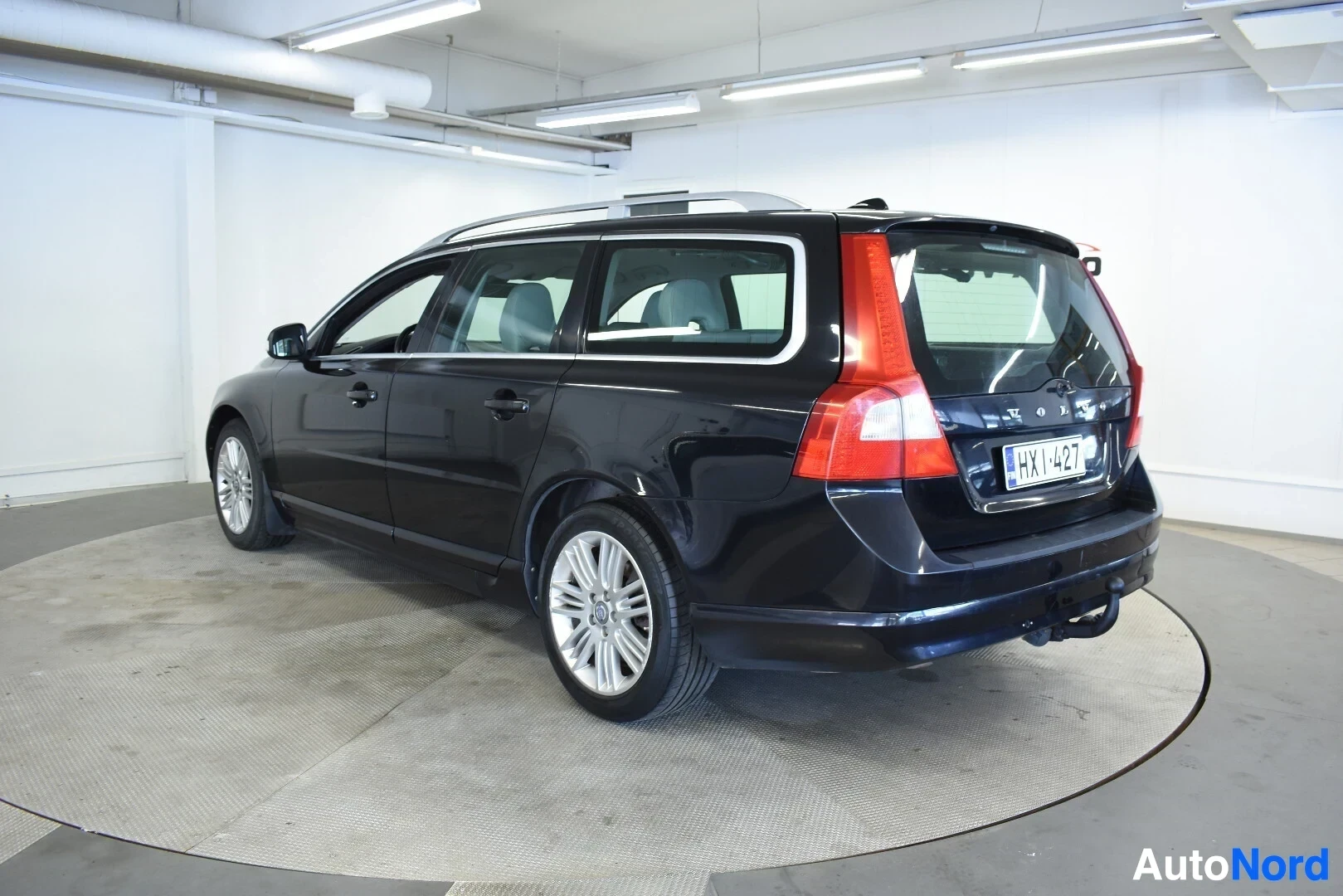 Takaviisto: Musta Volvo V70 -farmariauto takaviistosta kuvattuna sisätiloissa. Autossa on kattokiskot ja vetokoukku.