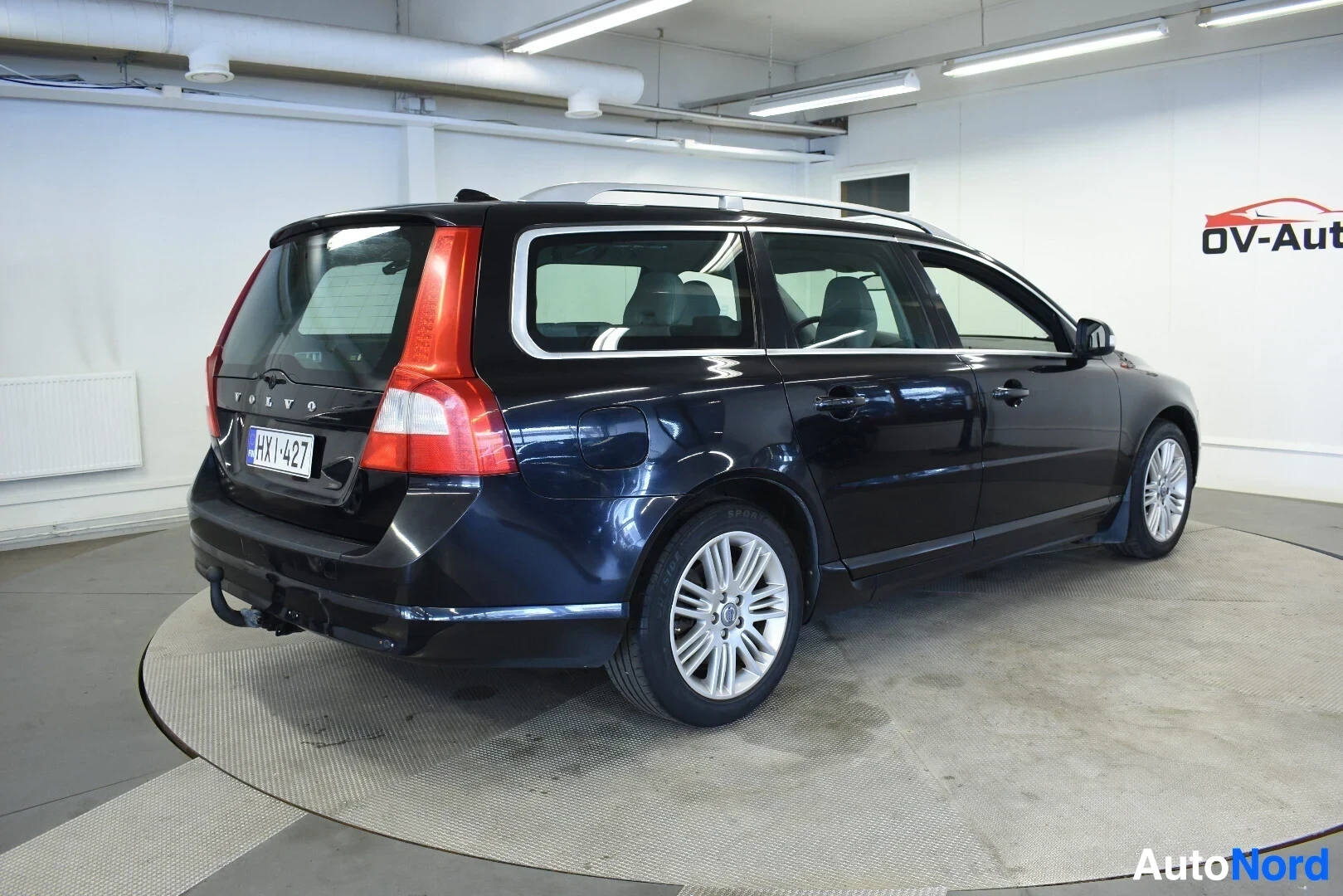 Takaviisto: Musta Volvo V70 -farmariauto takaviistosta kuvattuna sisätiloissa. Autossa on kattokiskot ja vetokoukku.