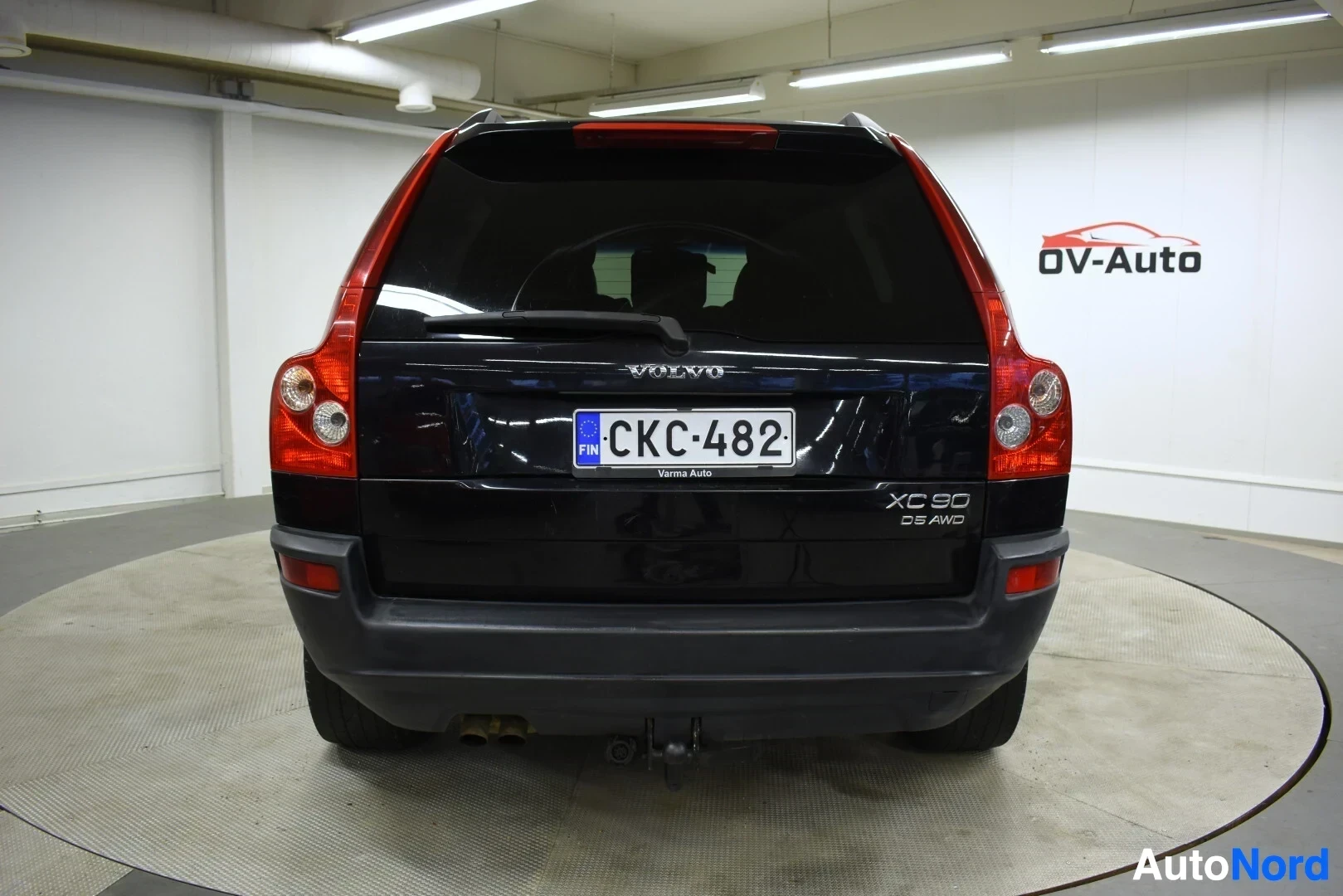 Takaa: Mustan Volvo XC90:n takaosa valkoisessa hallissa pyörivällä alustalla. Rekisterikilvessä on teksti ''