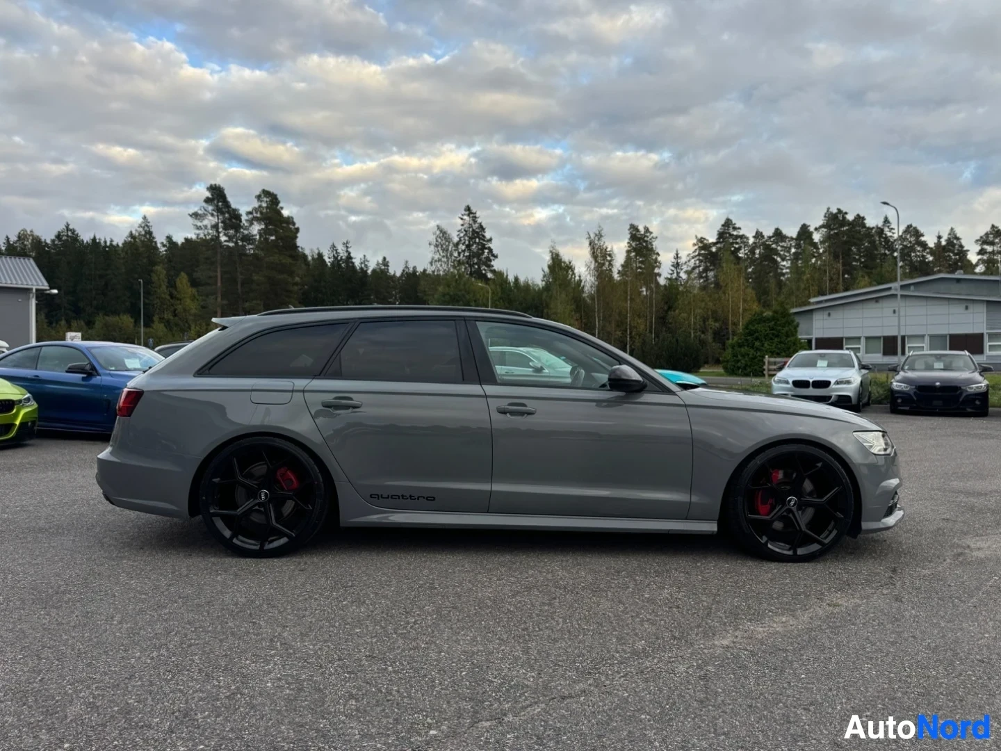 Sivulta: Harmaa farmariauto vasemmalta sivulta ulkona pysäköitynä. Autossa on mustat monipuolavanteet, joissa näkyy punaiset jarrusatulat. Kyljessä on "quattro"-teksti.